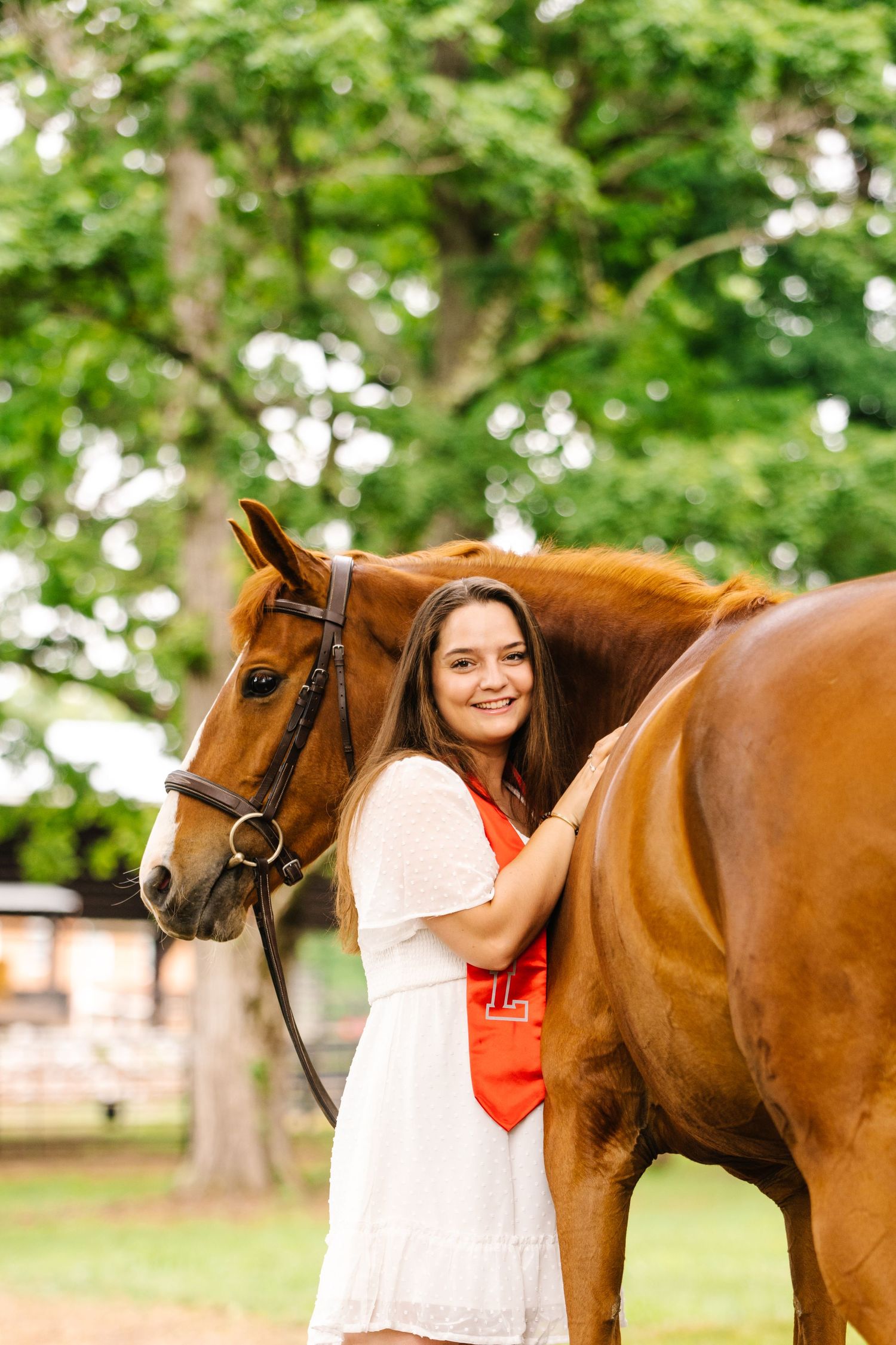 A chestnut horse wearing a bridle stands with its handler in a peaceful garden setting.