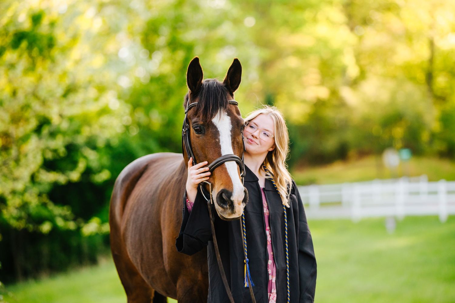 Person in black jacket stands with bay horse featuring white blaze in green pasture.