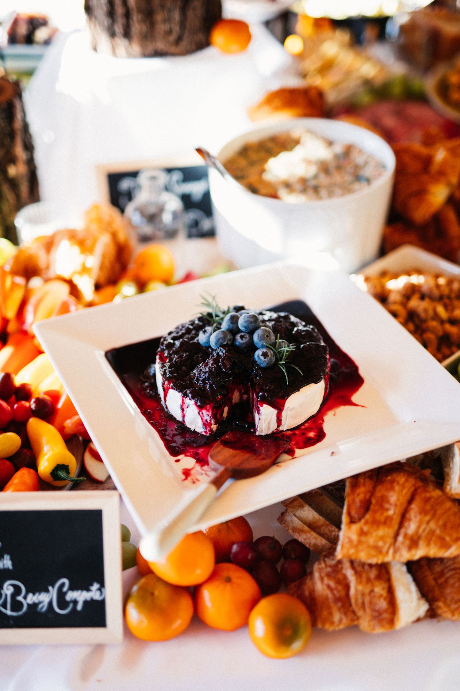 Gourmet cheese plate with blueberry compote alongside pastries and fruits at wedding reception.