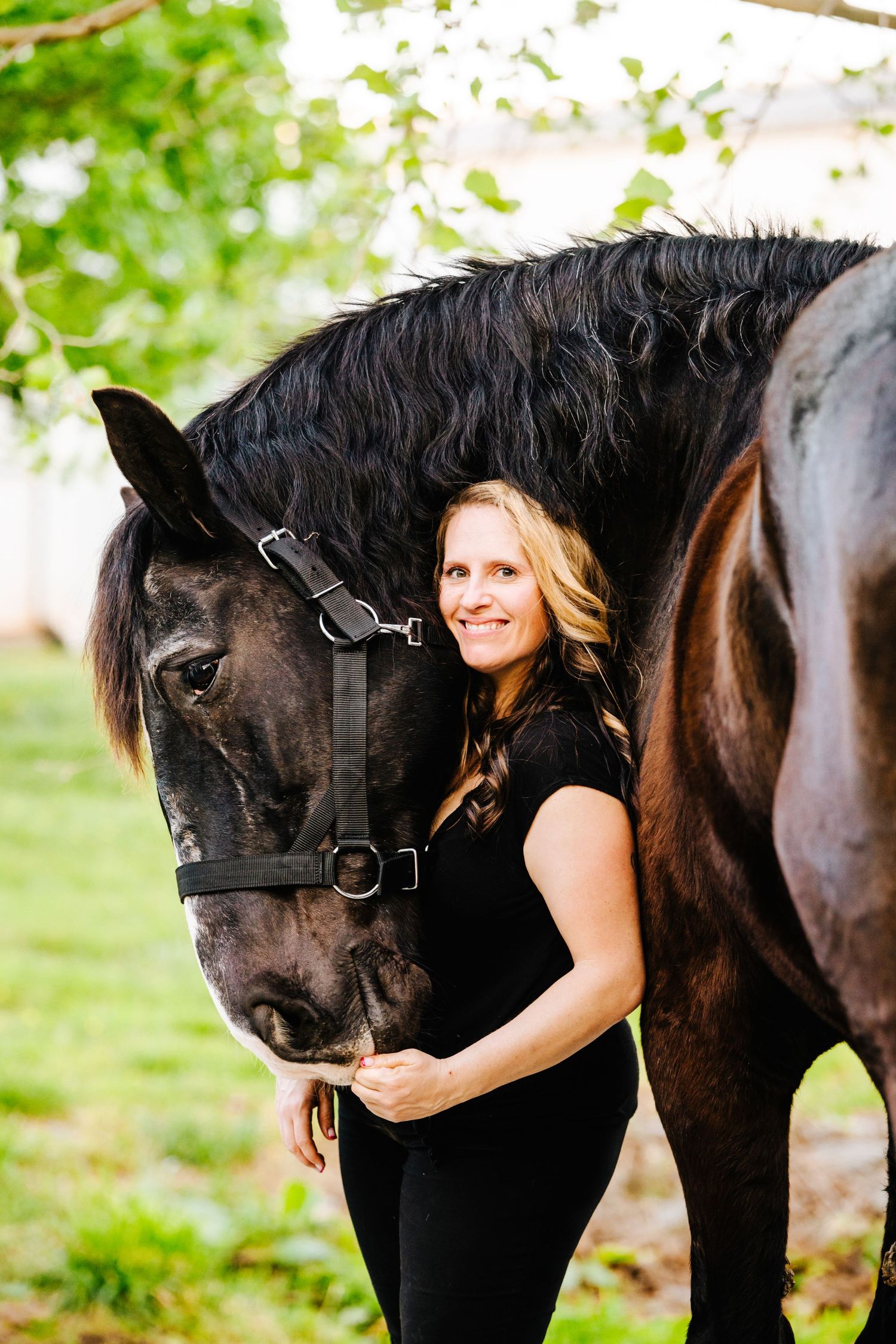 A magnificent black horse with flowing mane poses with its handler against a leafy green background.