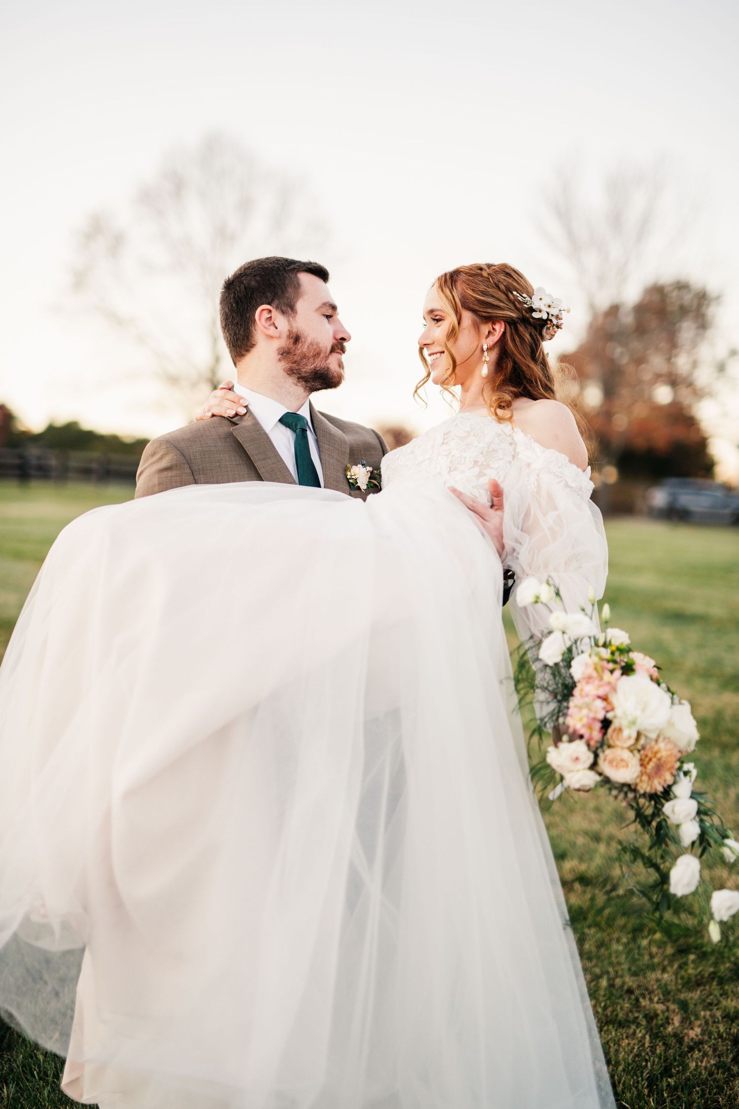 Wedding couple embracing in a sunlit field with flowing white dress.