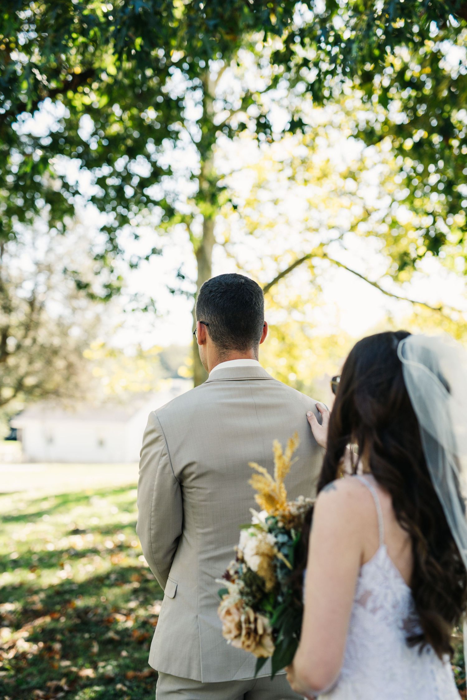 A couple in wedding attire is photographed from behind under golden fall foliage.
