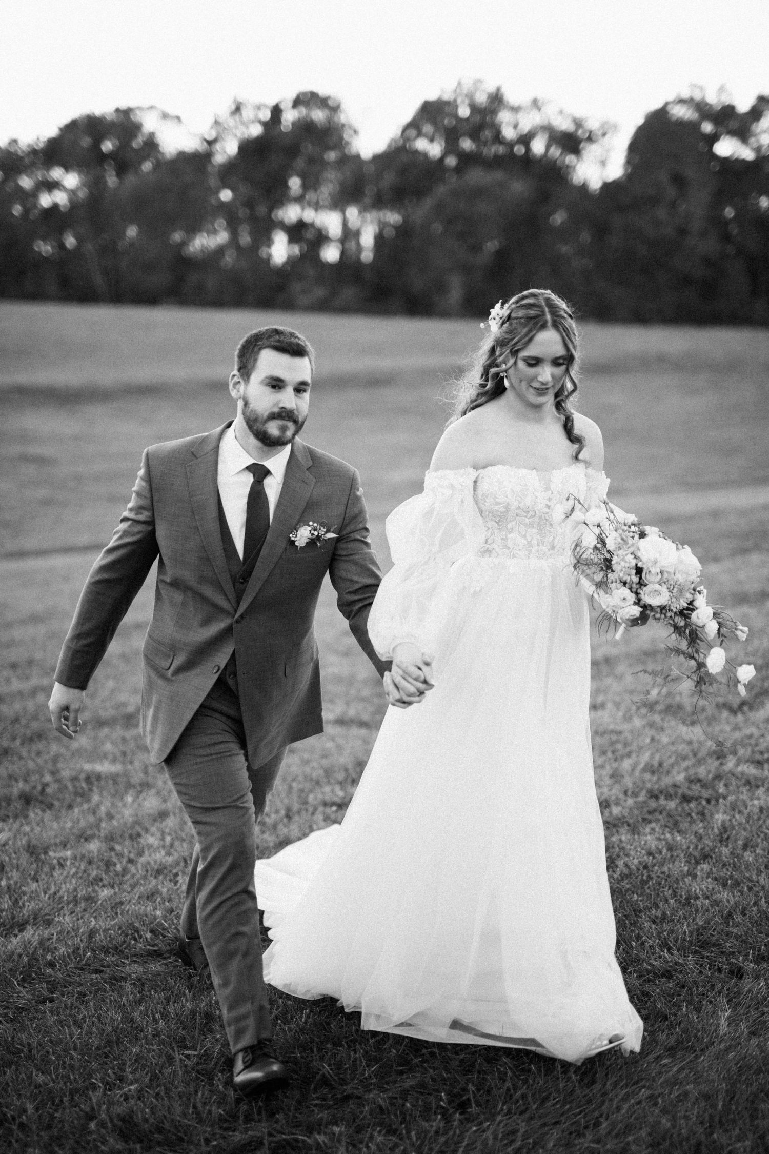 Black and white portrait of couple walking together across grassy field.