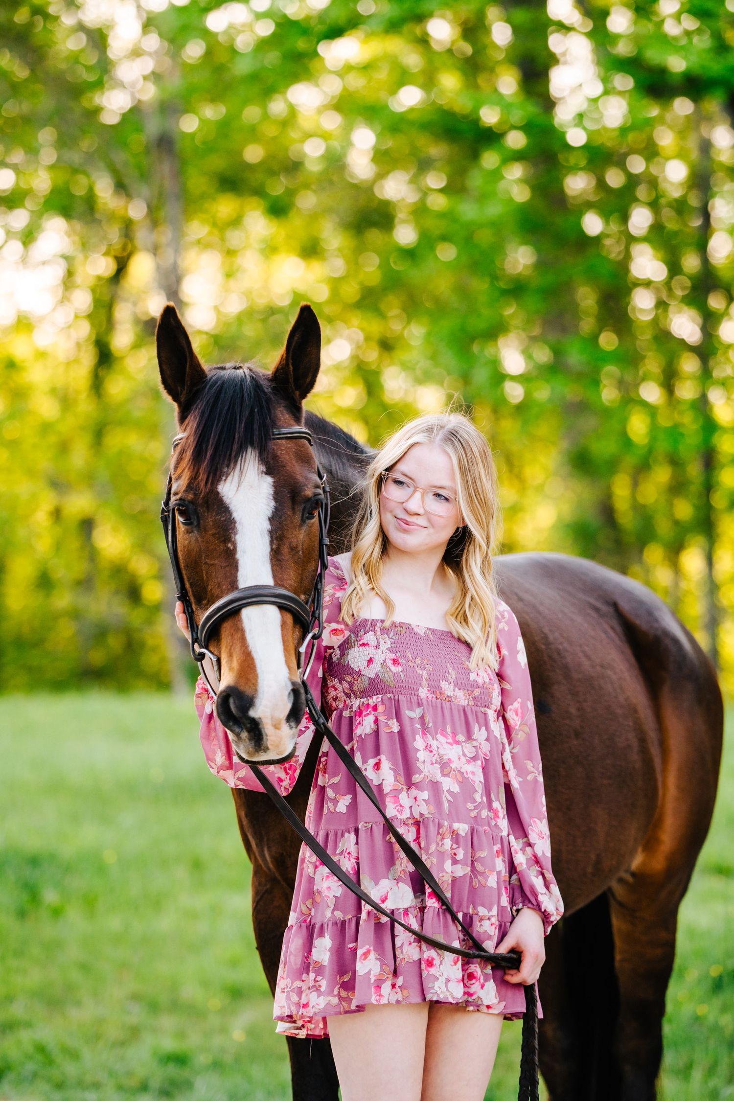 Bay horse and person in pink dress pose together against golden sunlit trees.