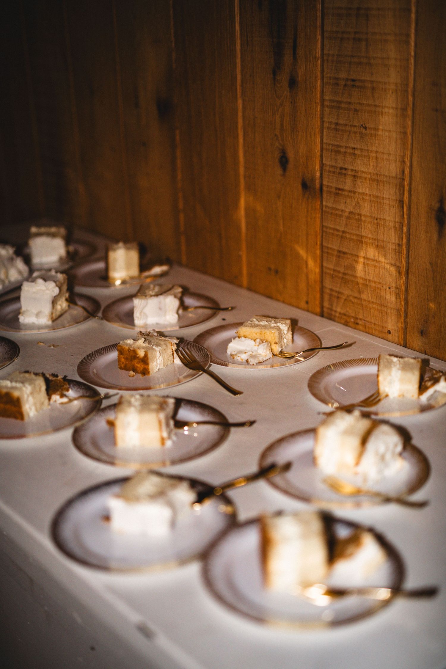 Individual servings of wedding cake plated on white dishes in a rustic wooden venue.
