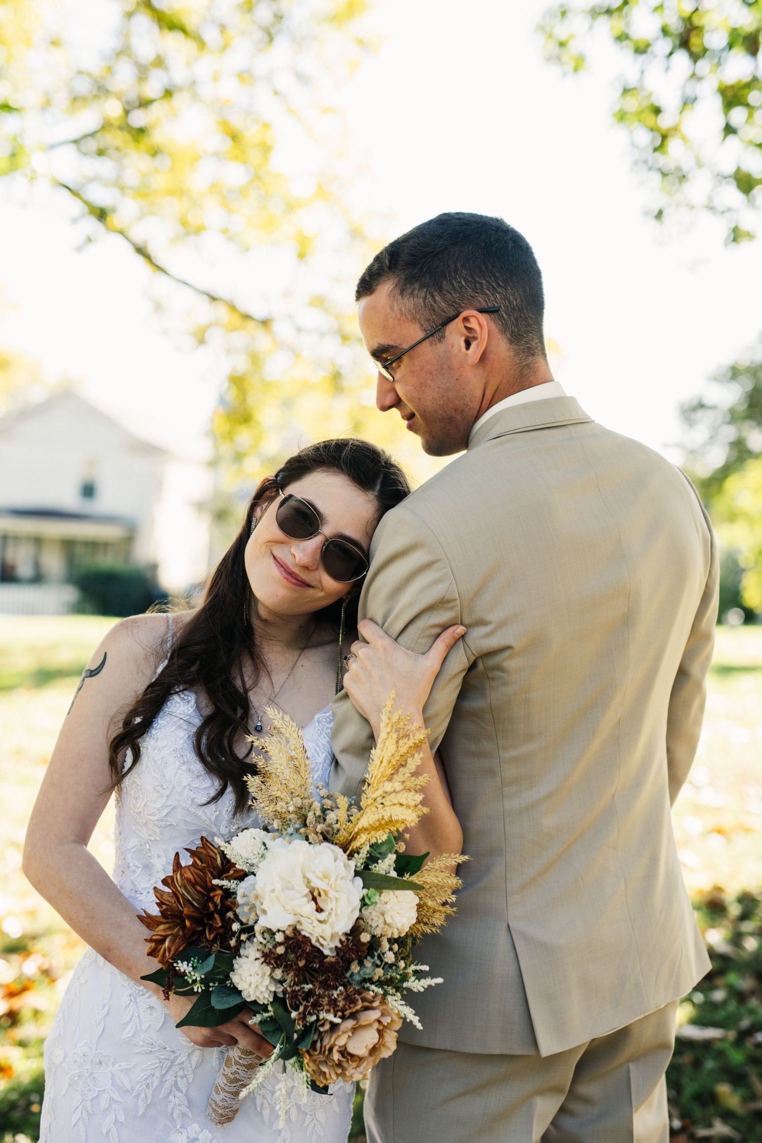 Newlyweds share intimate moment in sunlit garden with bride holding fall-themed floral bouquet.