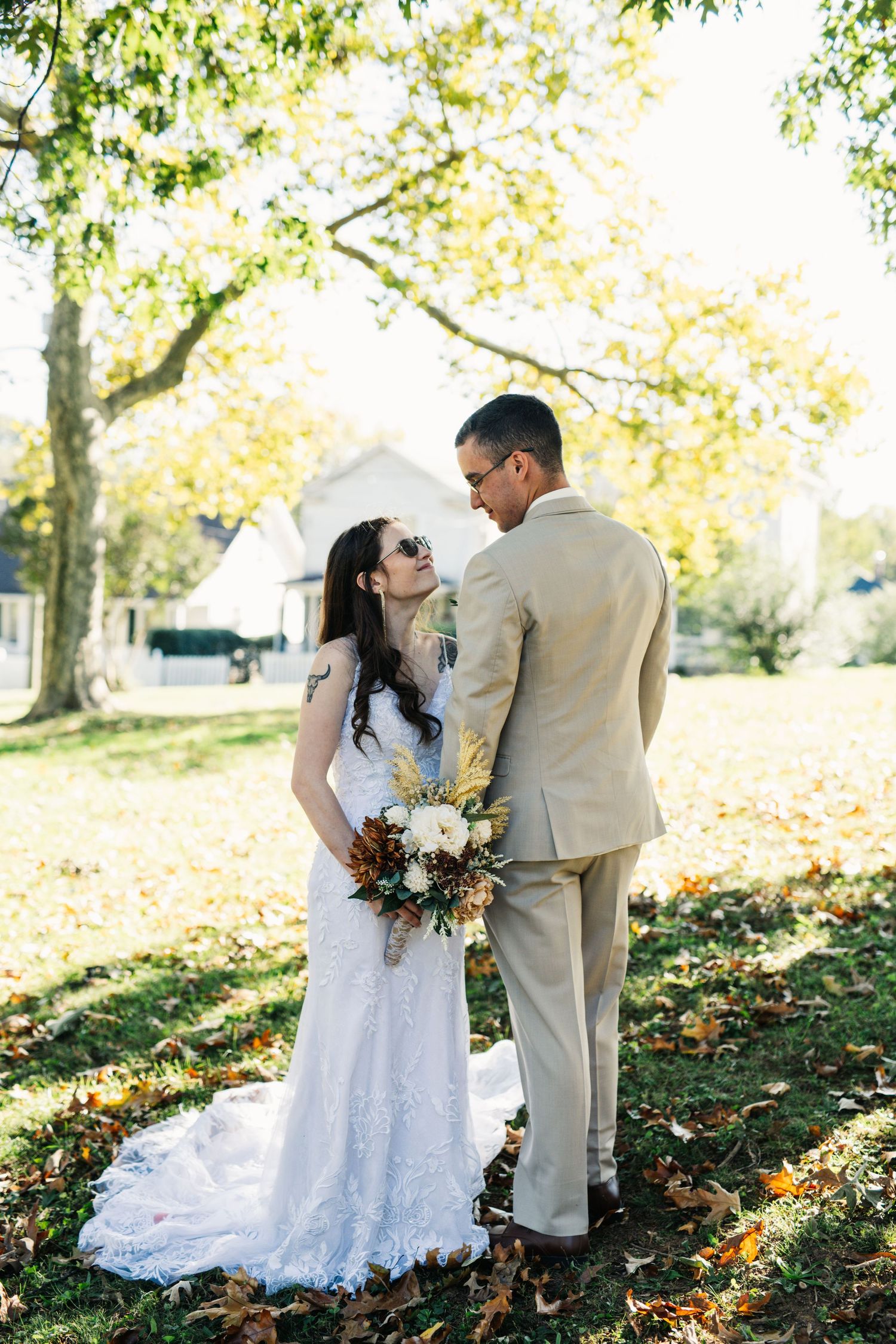 A wedding couple poses together on fallen autumn leaves while holding a rustic bouquet.