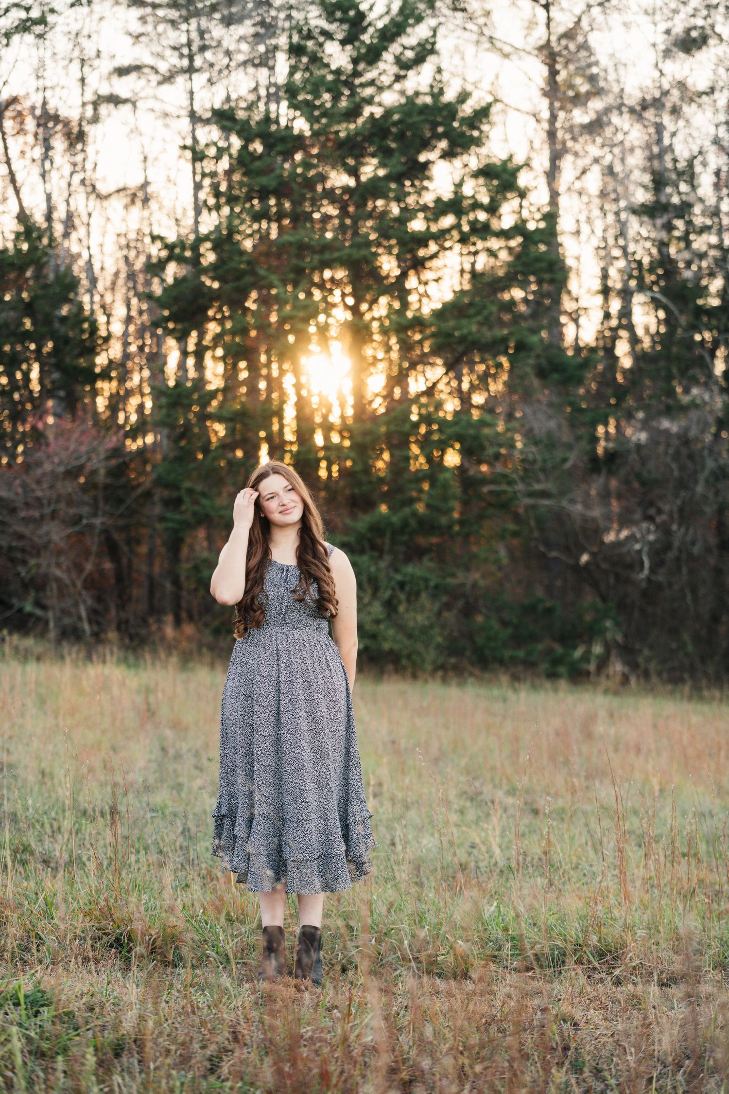 A sunset photoshoot in a rustic field with pine trees silhouetted in the background.
