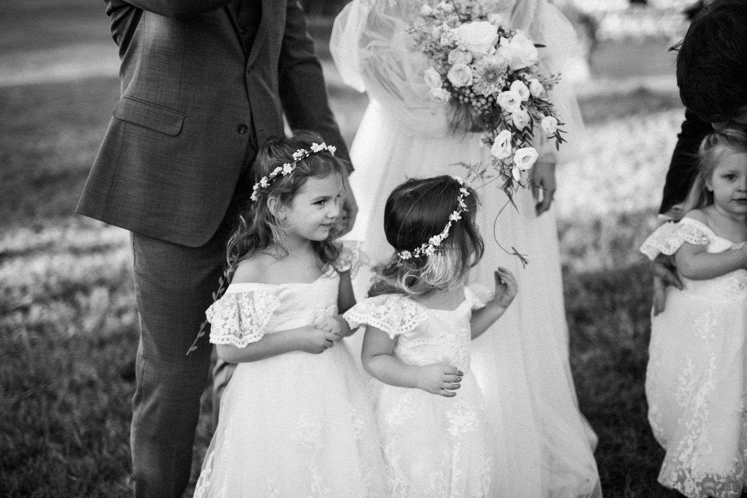 Young flower girls in white dresses share a moment at wedding ceremony.