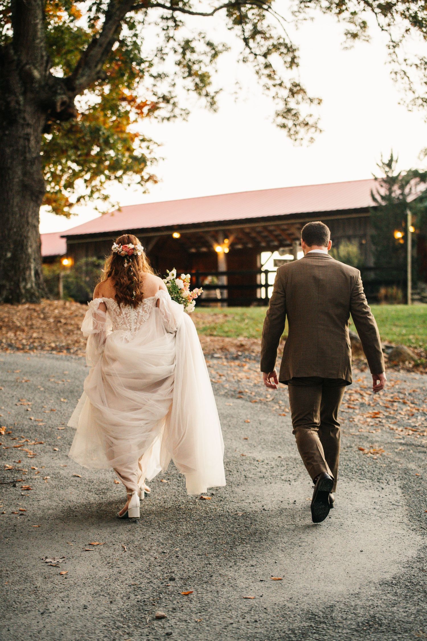 A bride and groom walking down a path towards a rustic barn venue on their wedding day.