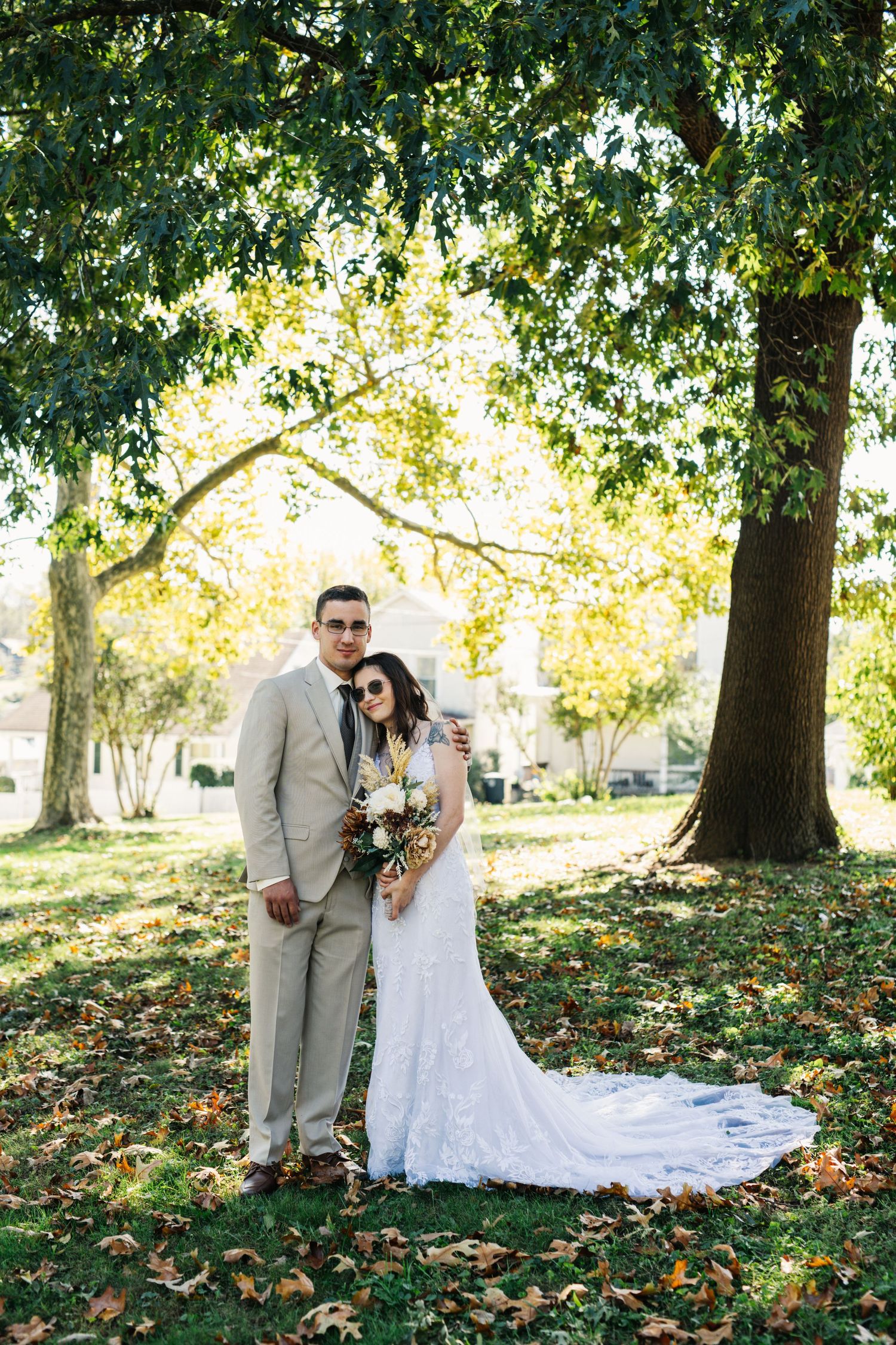 A wedding couple poses for portraits on grass covered with fall leaves.