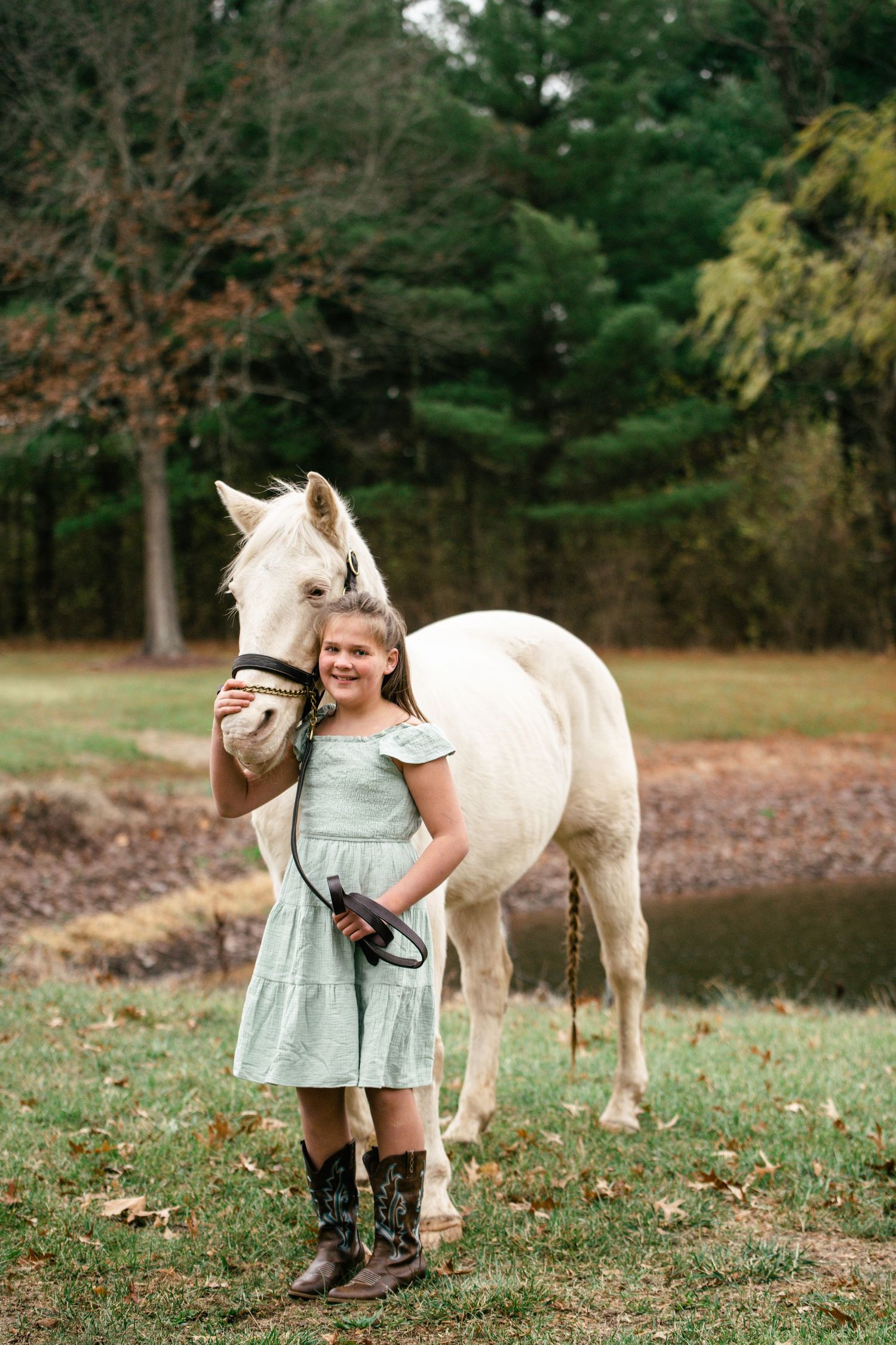 A beautiful white horse stands with a companion in a mint dress against a wooded background.