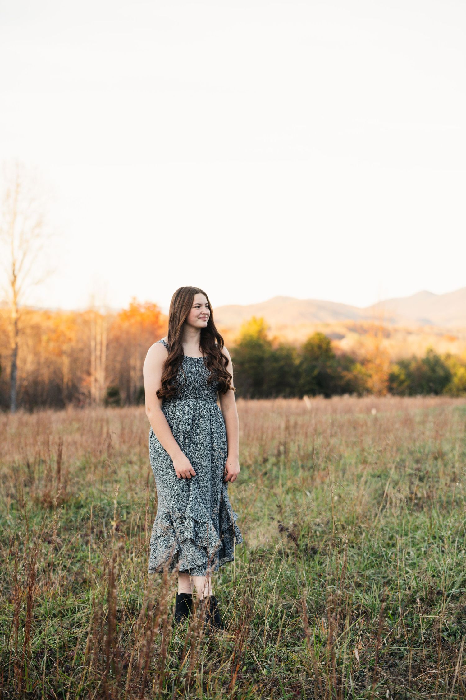 A person in a floral dress stands in a sunlit autumn field at golden hour.