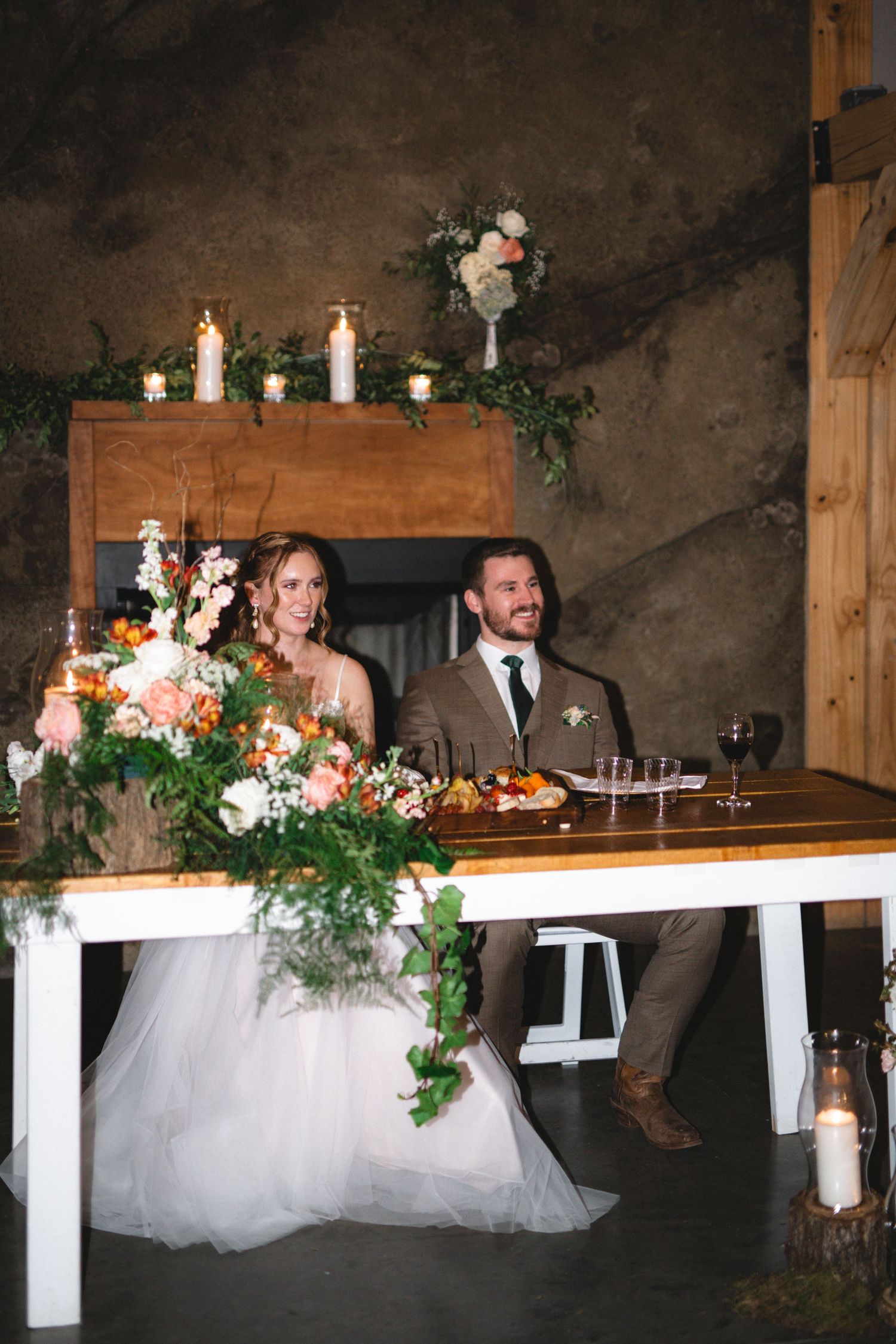 A sweetheart table decorated with candles and floral arrangements at a rustic wedding reception.