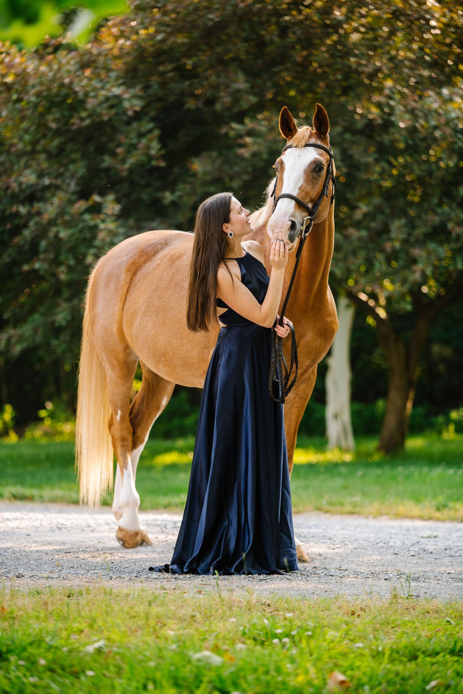A palomino horse and formal dressed companion share a moment on a tree-lined path.