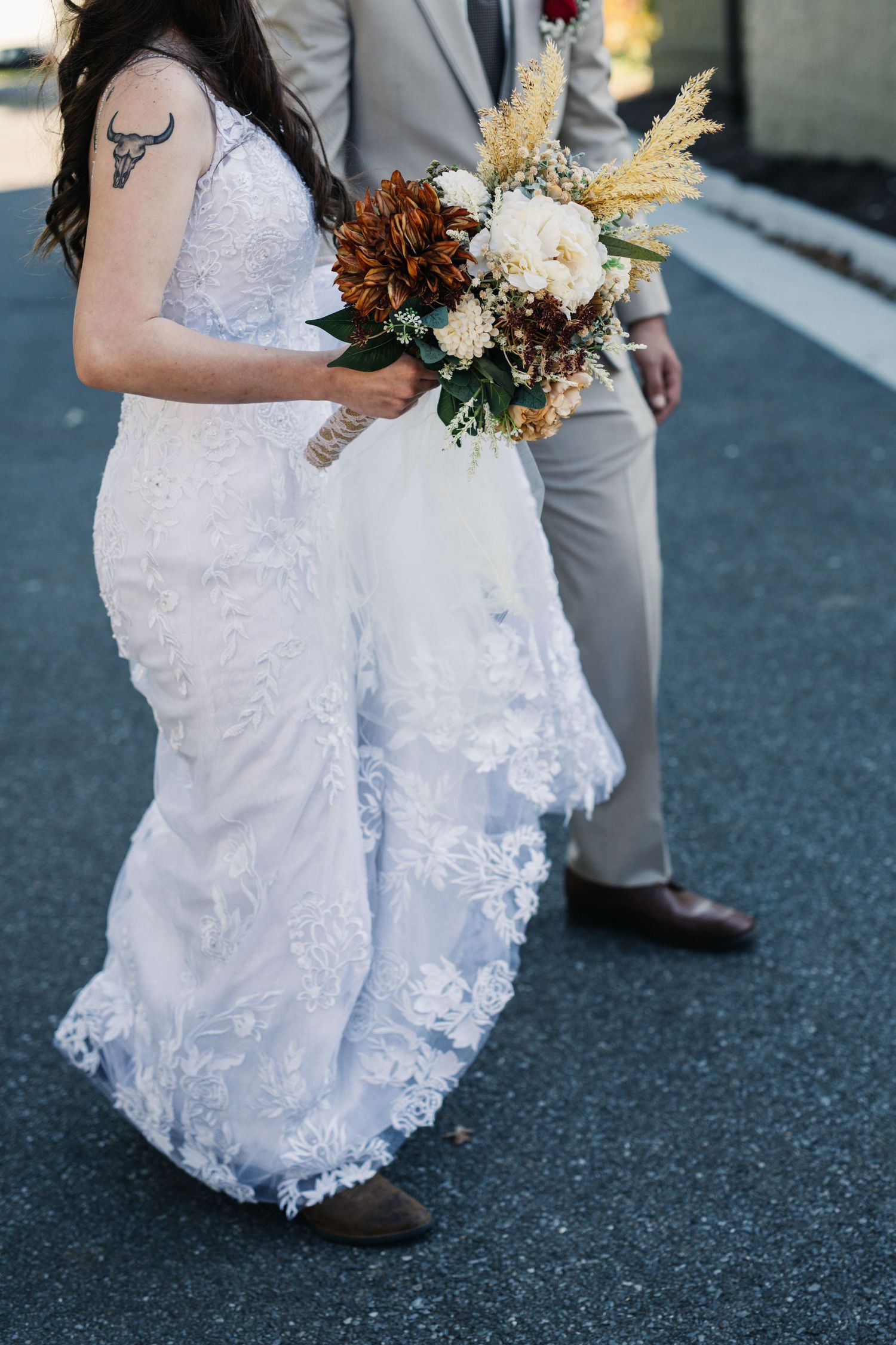 Close-up of bride in lace dress holding rustic bouquet with dried flowers.