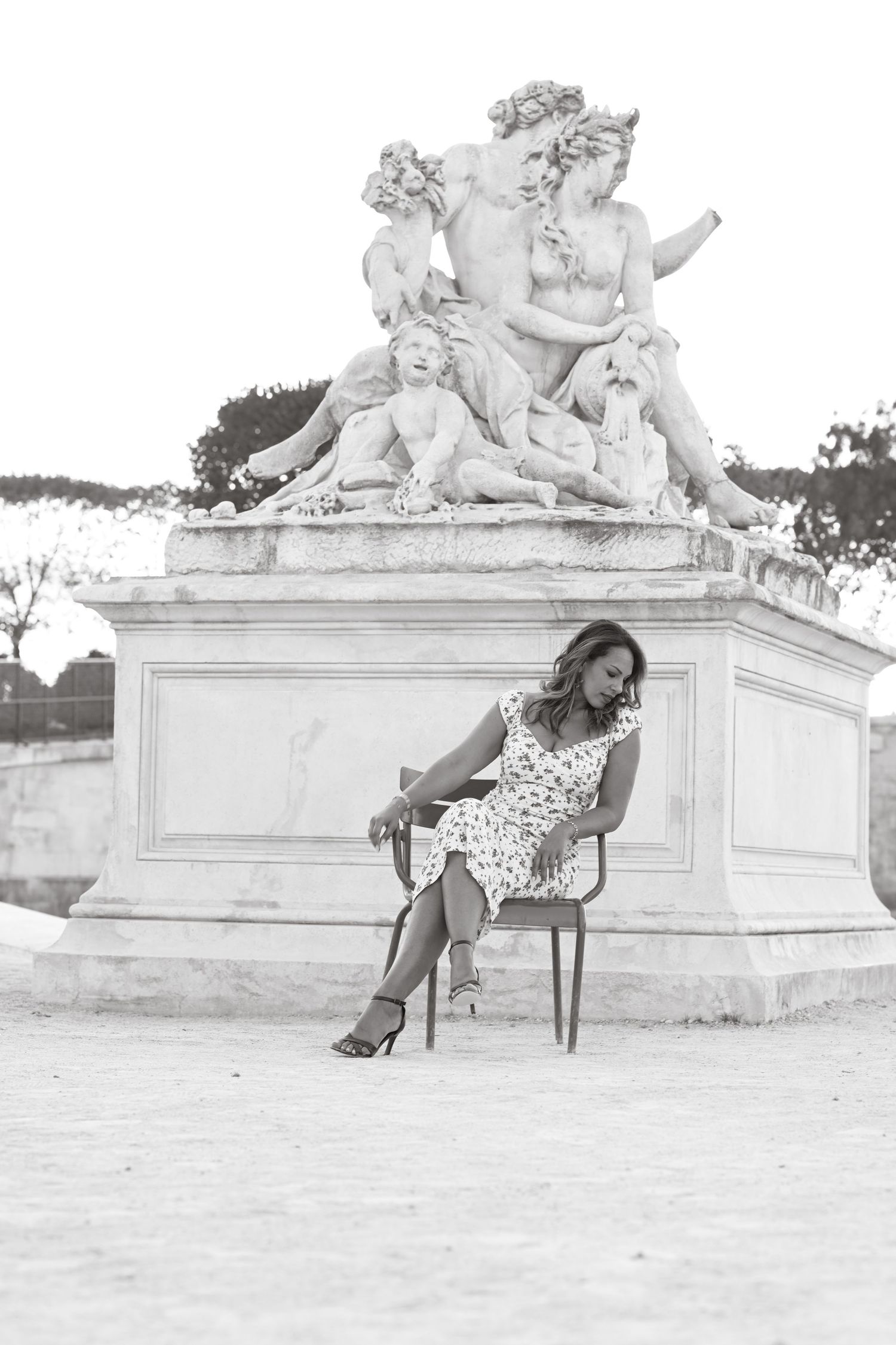 A black and white photo featuring a classical statue and chair in a Parisian setting.