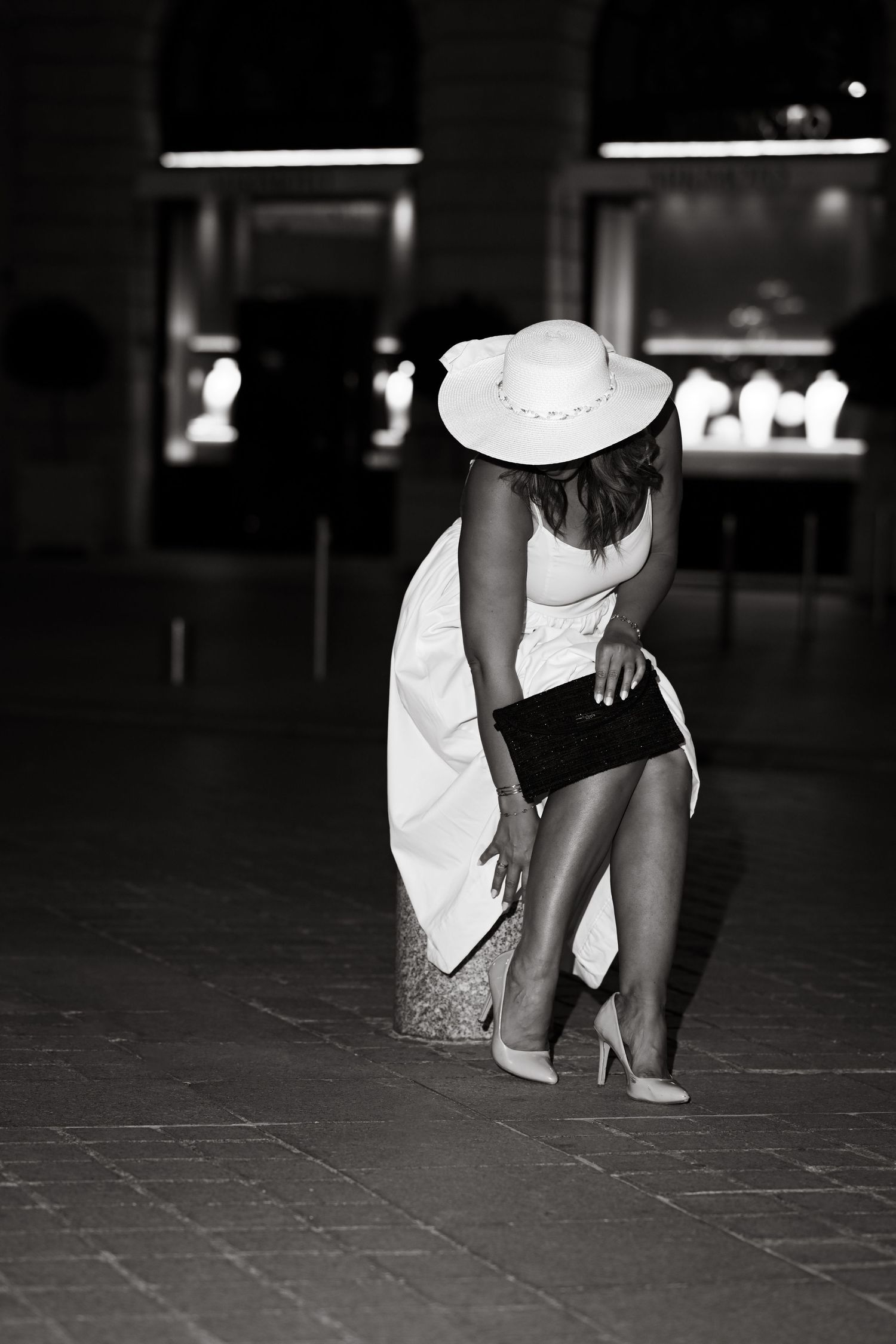 Black and white fashion portrait with dramatic pose in white dress and hat.
