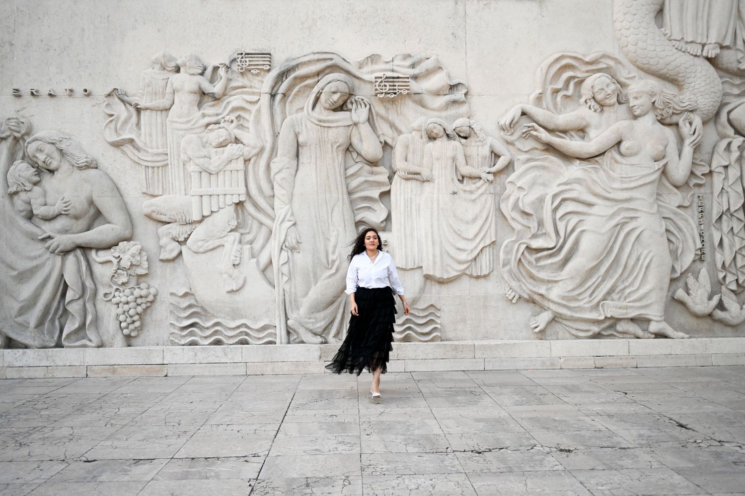 Fashion portrait against dramatic stone wall relief featuring classical figures.