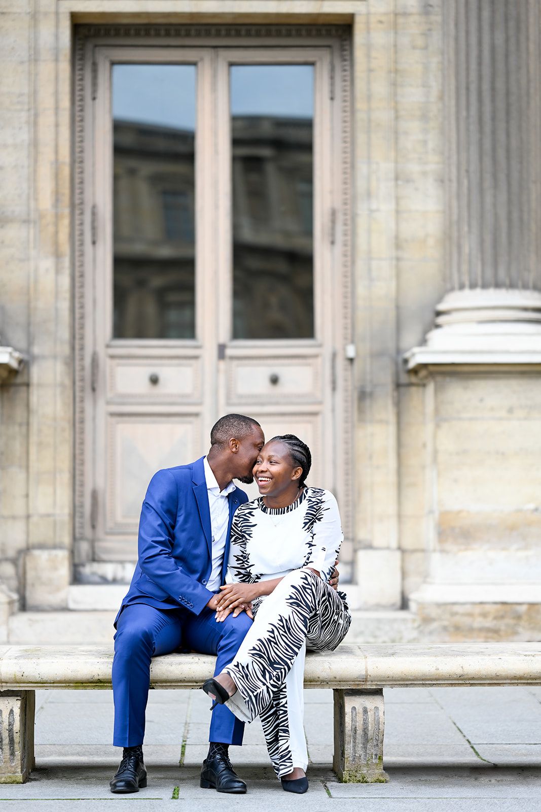 A couple shares a tender moment on steps of a classical building.