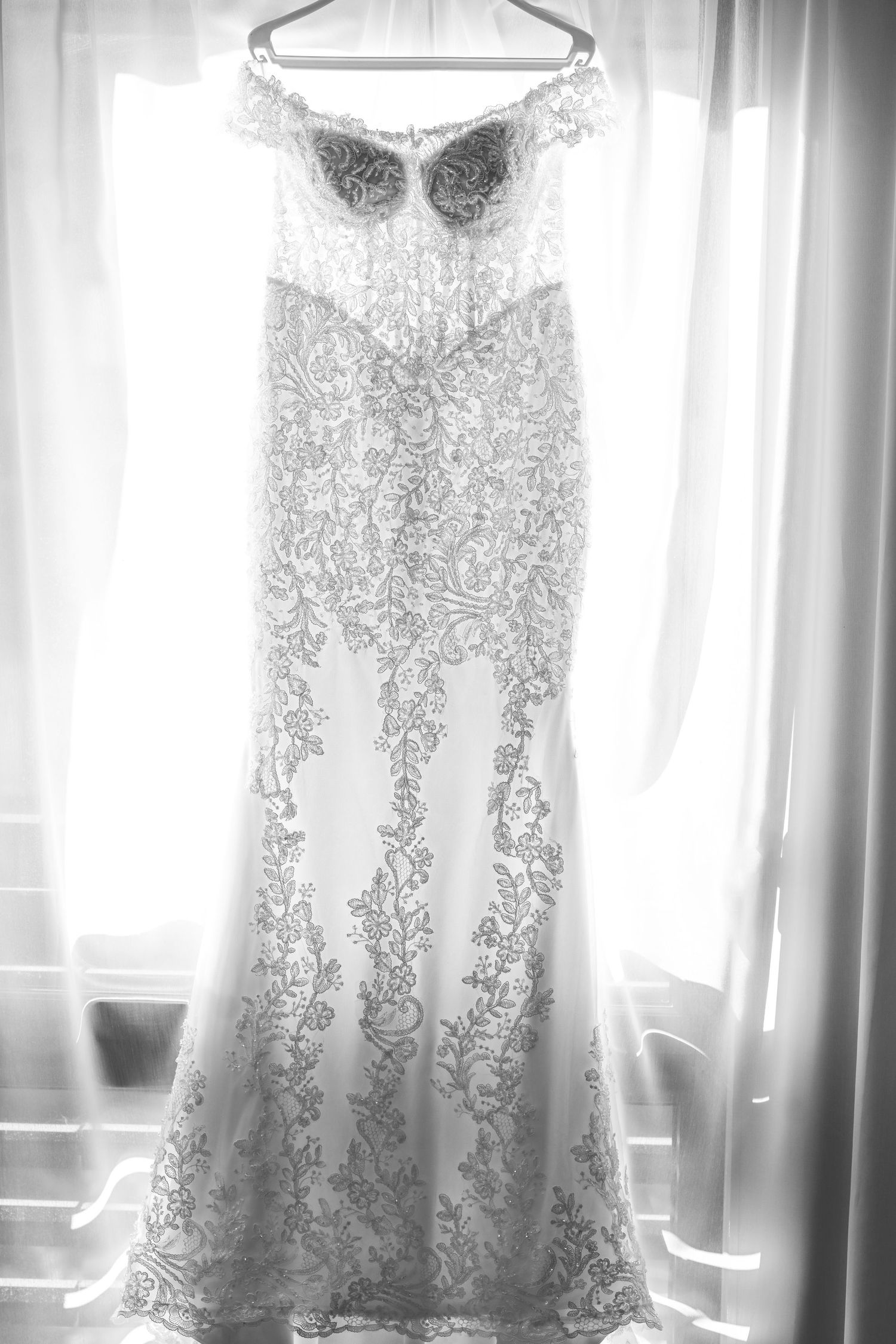 Elegant lace wedding dress hanging in front of bright windows creating a dreamy silhouette.
