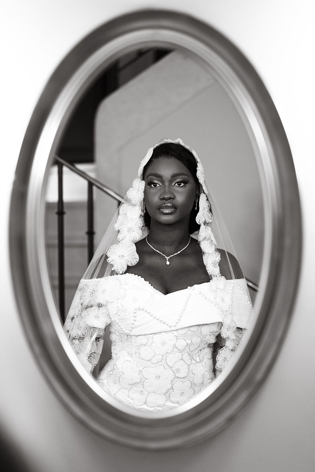 Stunning black and white portrait of a bride in a lace wedding dress reflected in an oval mirror.