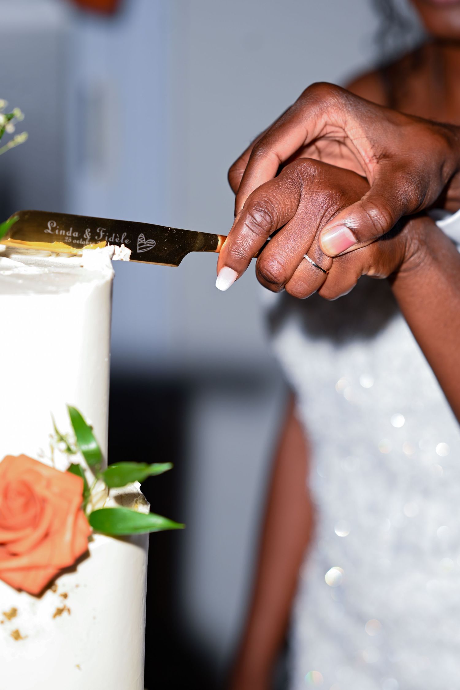 Detailed shot of hands holding knife while cutting white wedding cake.