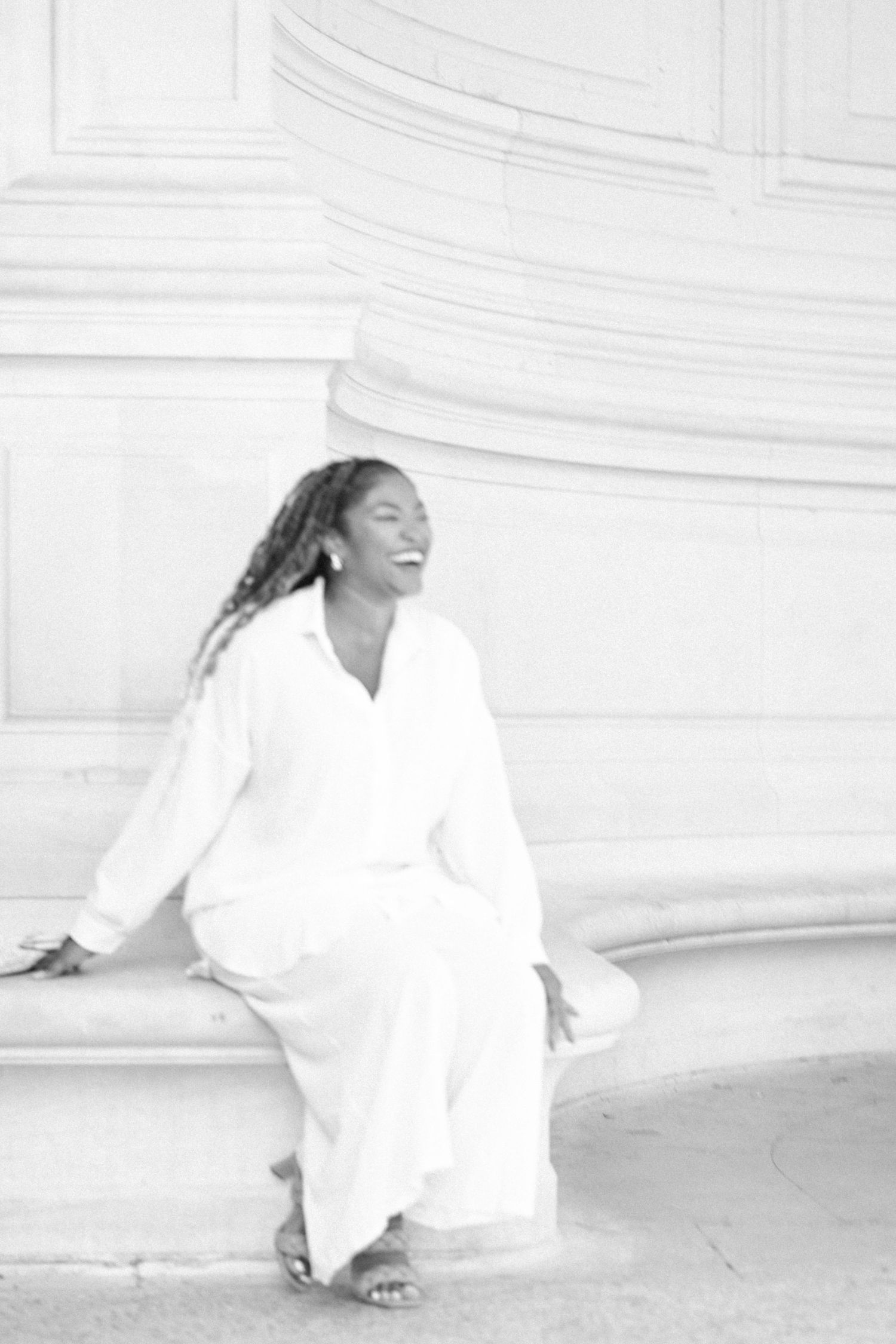 Person in flowing white dress poses gracefully against white architectural columns.