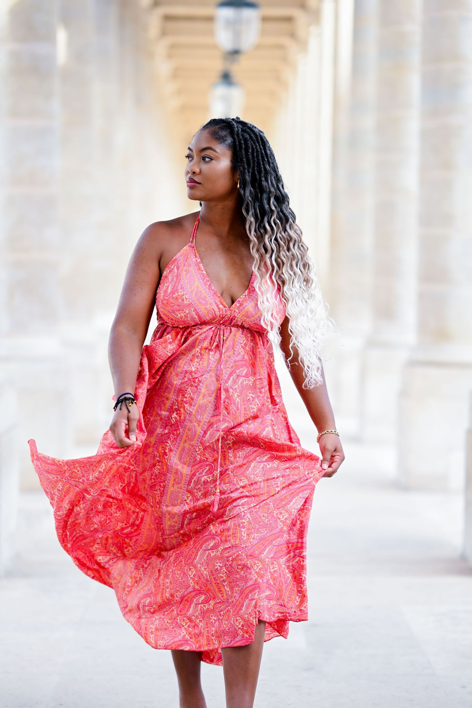 A coral paisley print maxi dress flows gracefully between classical stone columns.