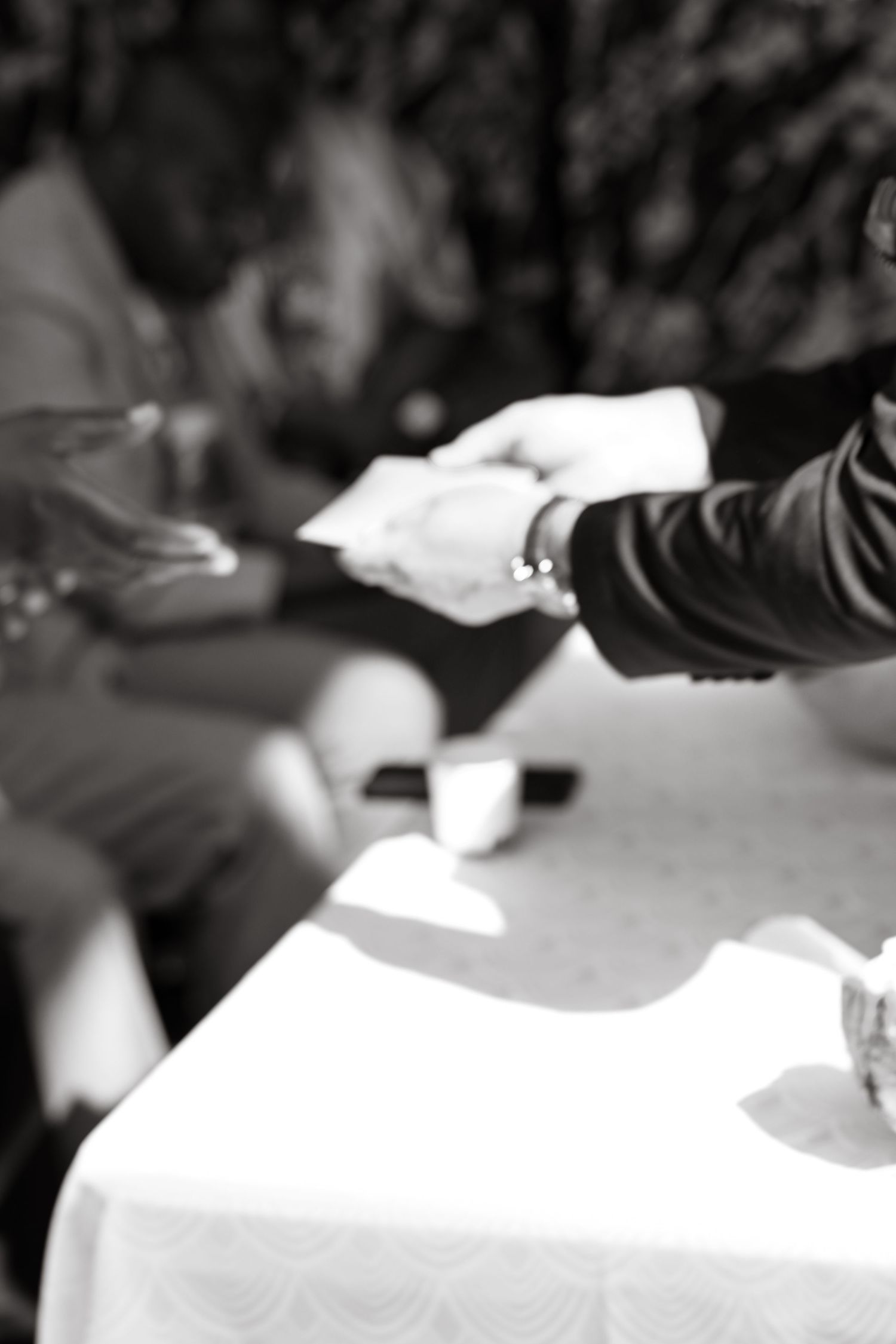 Black and white close-up of hands signing documents on a white tablecloth.