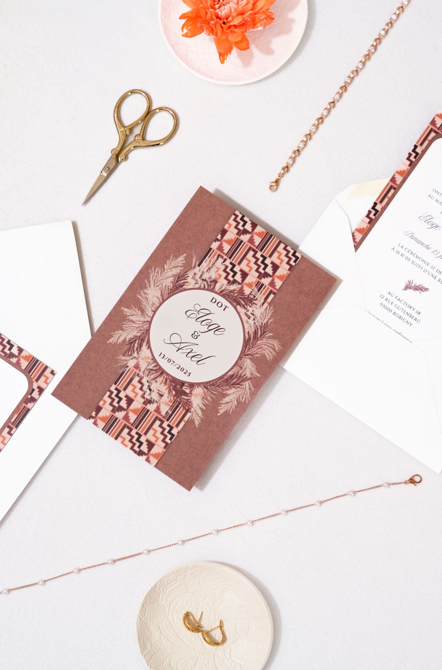 Wedding stationery flat lay with rose gold details and floral accents on white background.