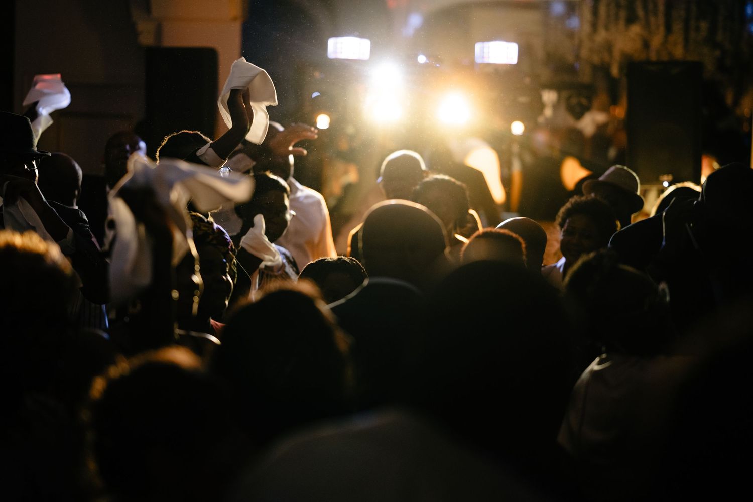 Silhouette of crowd at nighttime event with bright lights in background.