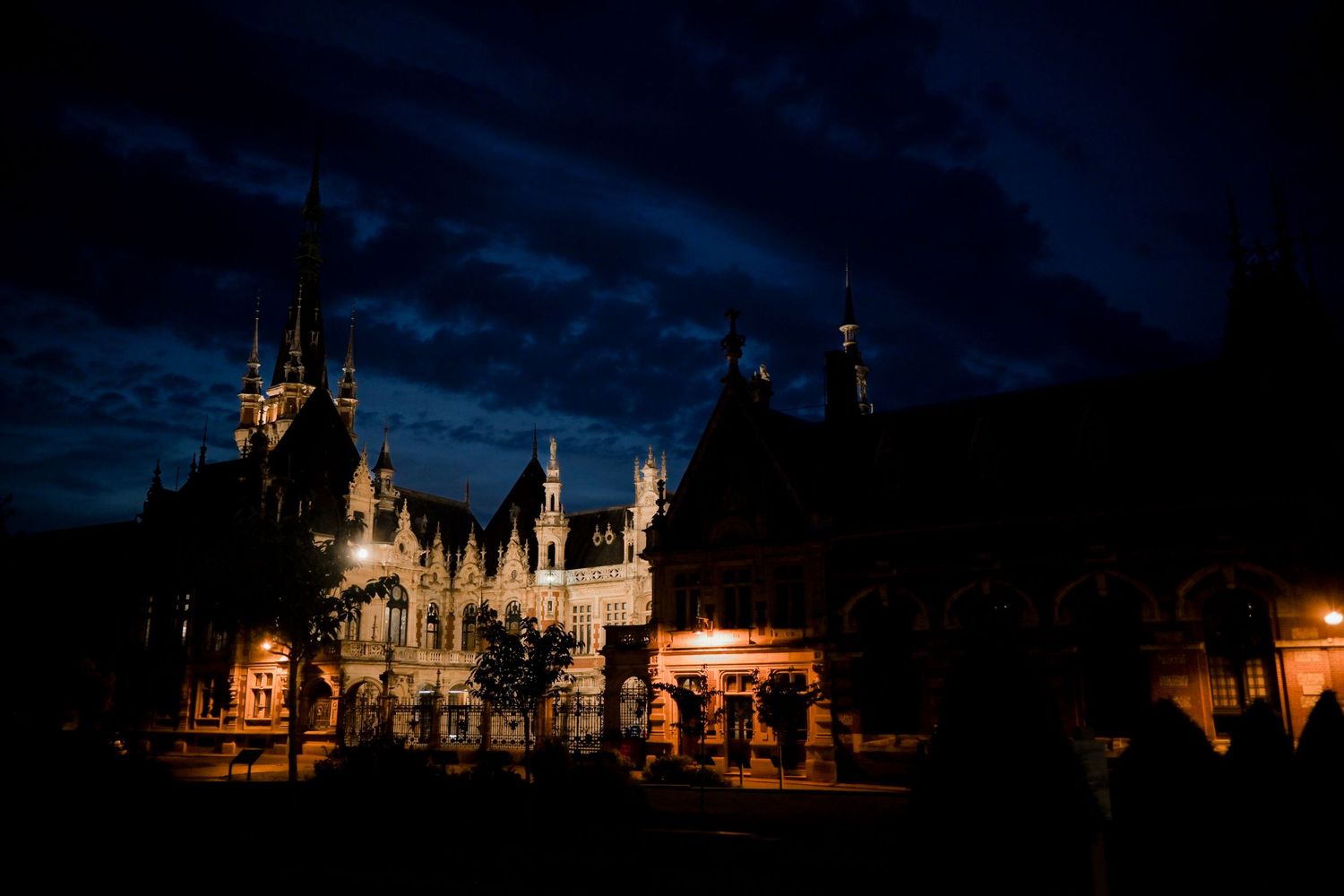 Gothic castle illuminated at night with dramatic dark blue sky.