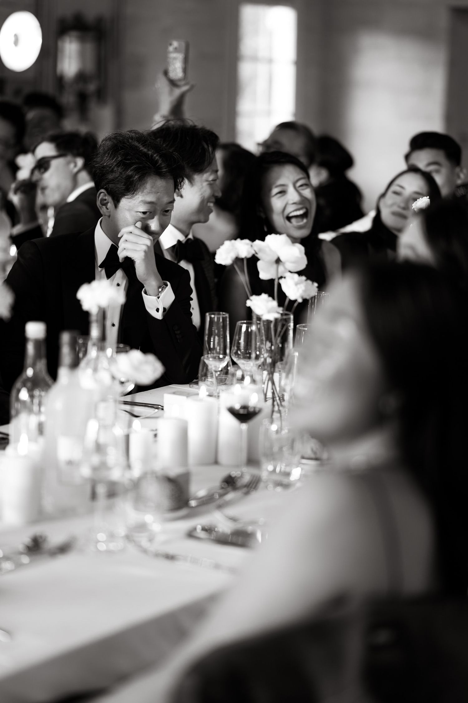Black and white photo of guests laughing during formal dinner reception.
