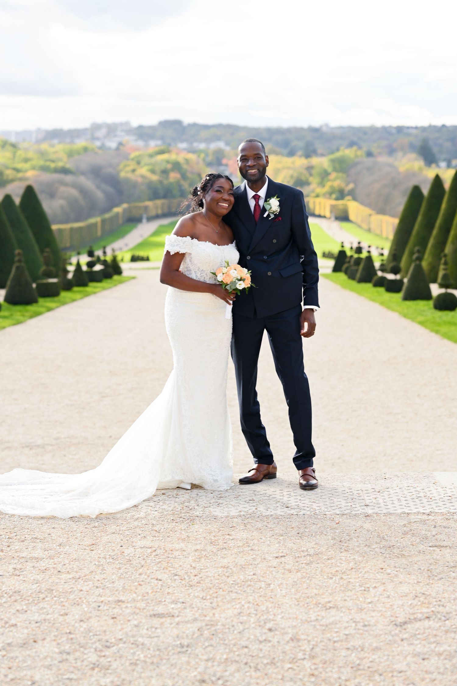 Wedding couple walks along a scenic garden path surrounded by manicured hedges.