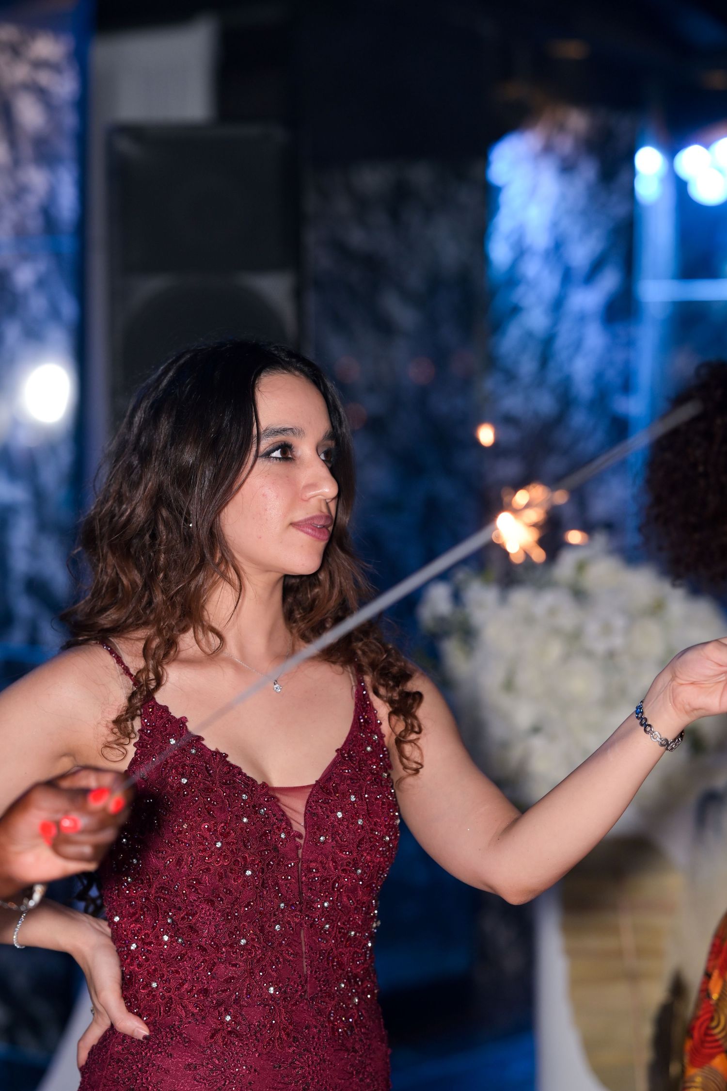 A person in a sparkly burgundy dress dances with sparklers at a celebration.