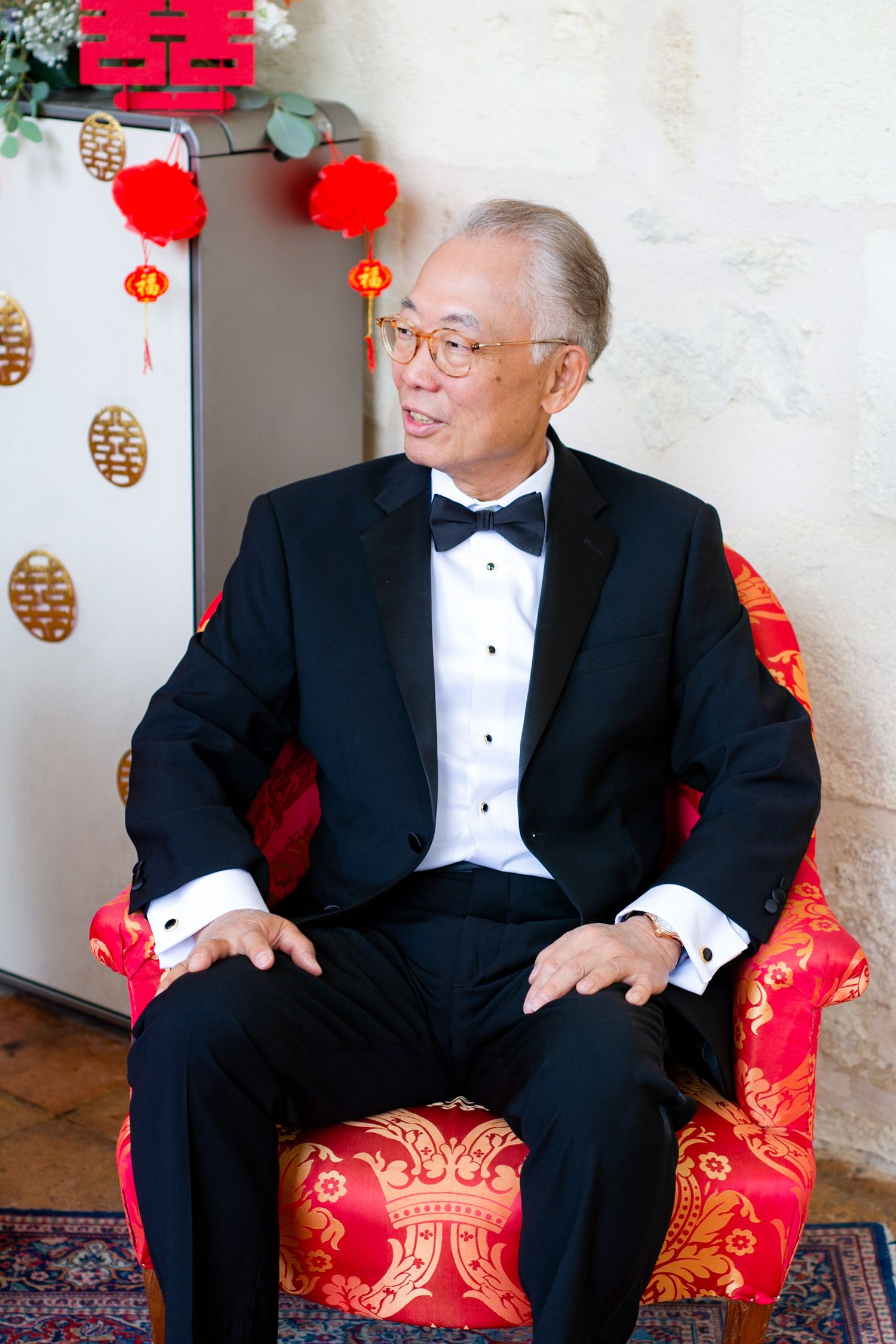 Formal portrait in front of traditional Chinese decorations with red lanterns and double happiness symbol.