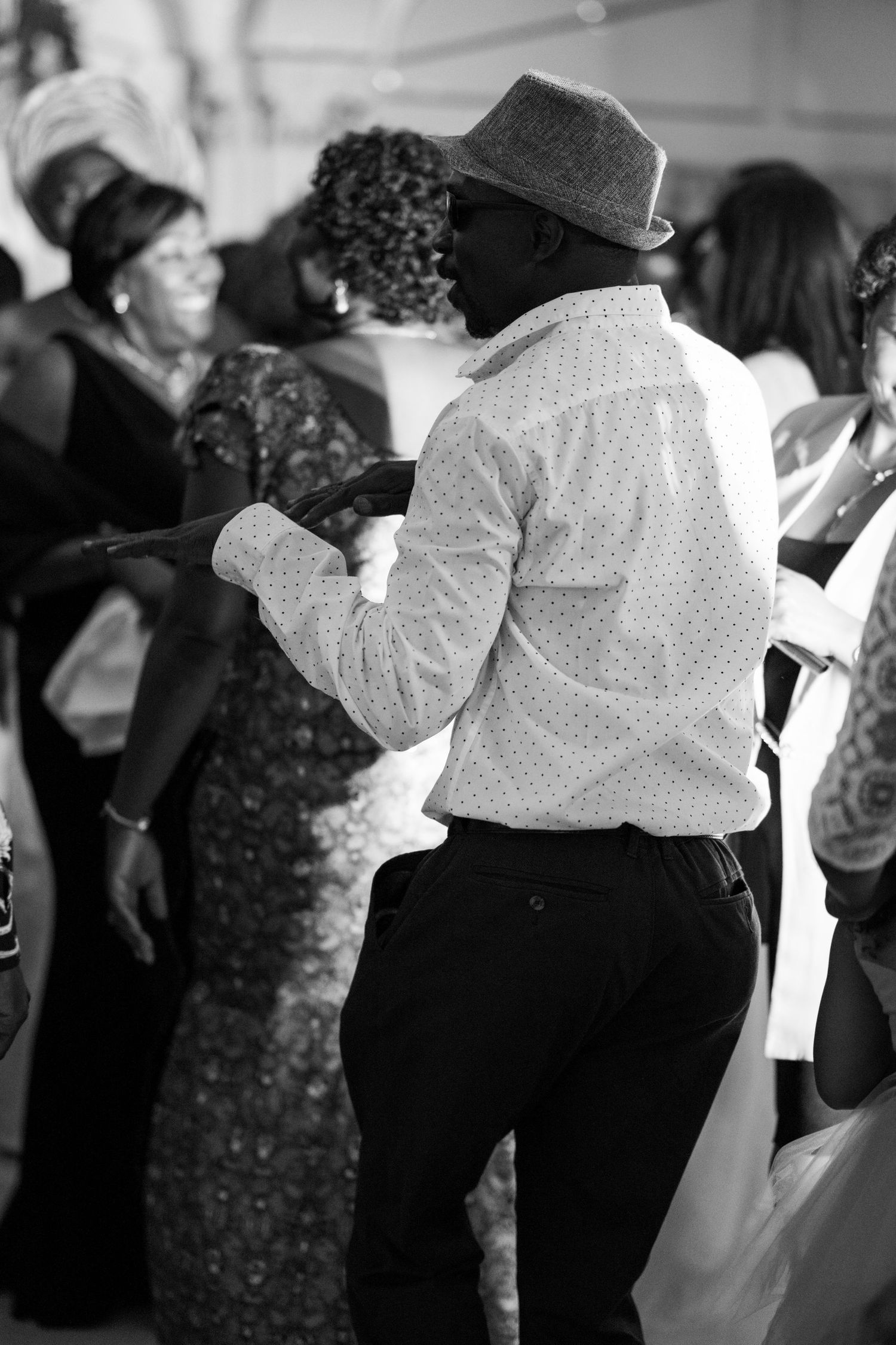 Person in fedora and polka dot shirt dancing at formal gathering.