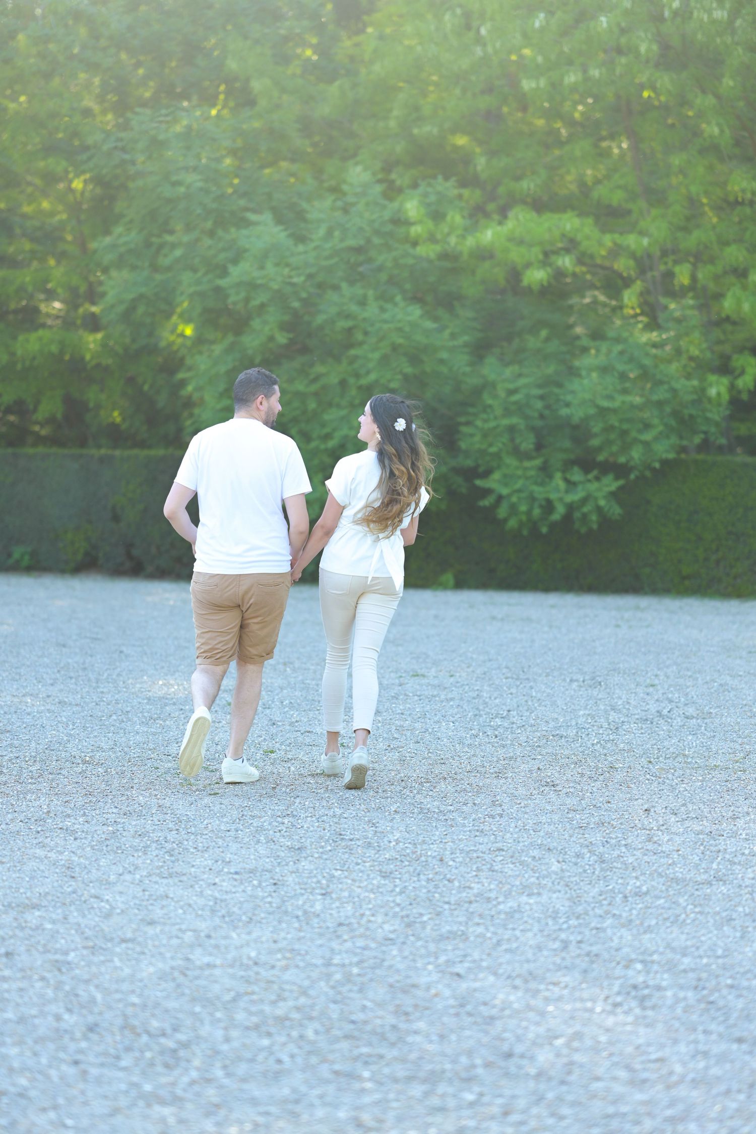 Distant view of couple walking together on gravel path surrounded by greenery.