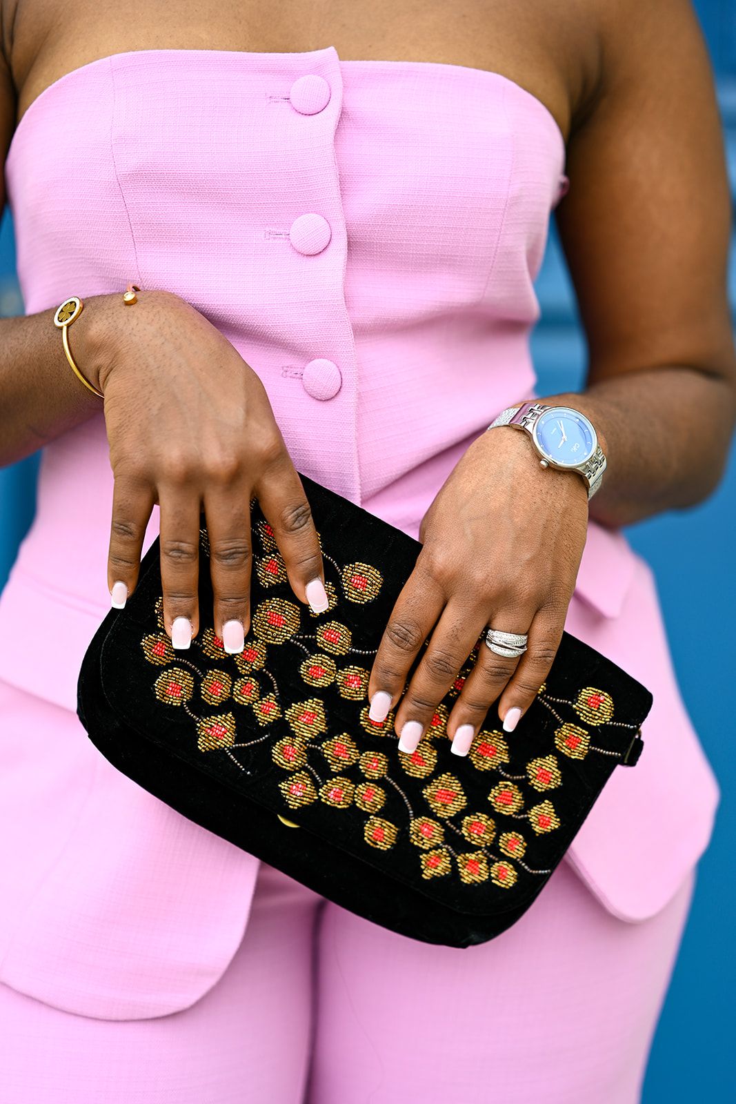 Embellished black clutch purse with floral details held against pink outfit with jewelry accents.