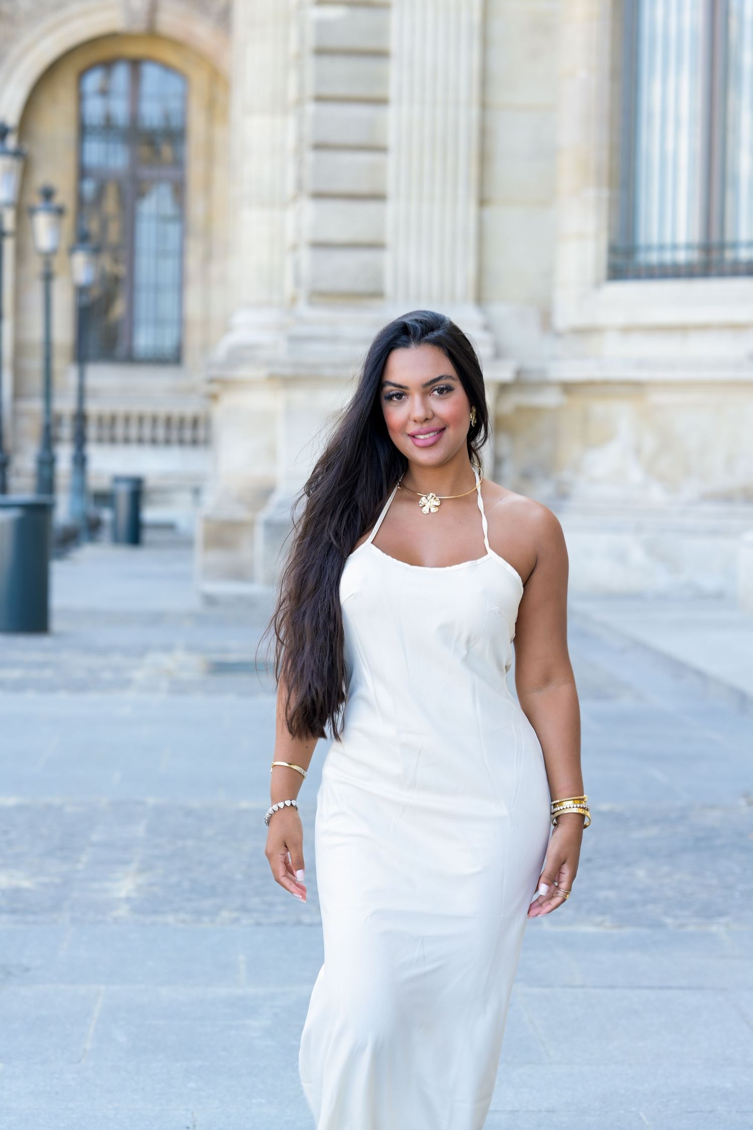 A person in a white maxi dress poses in front of an ornate European building facade.