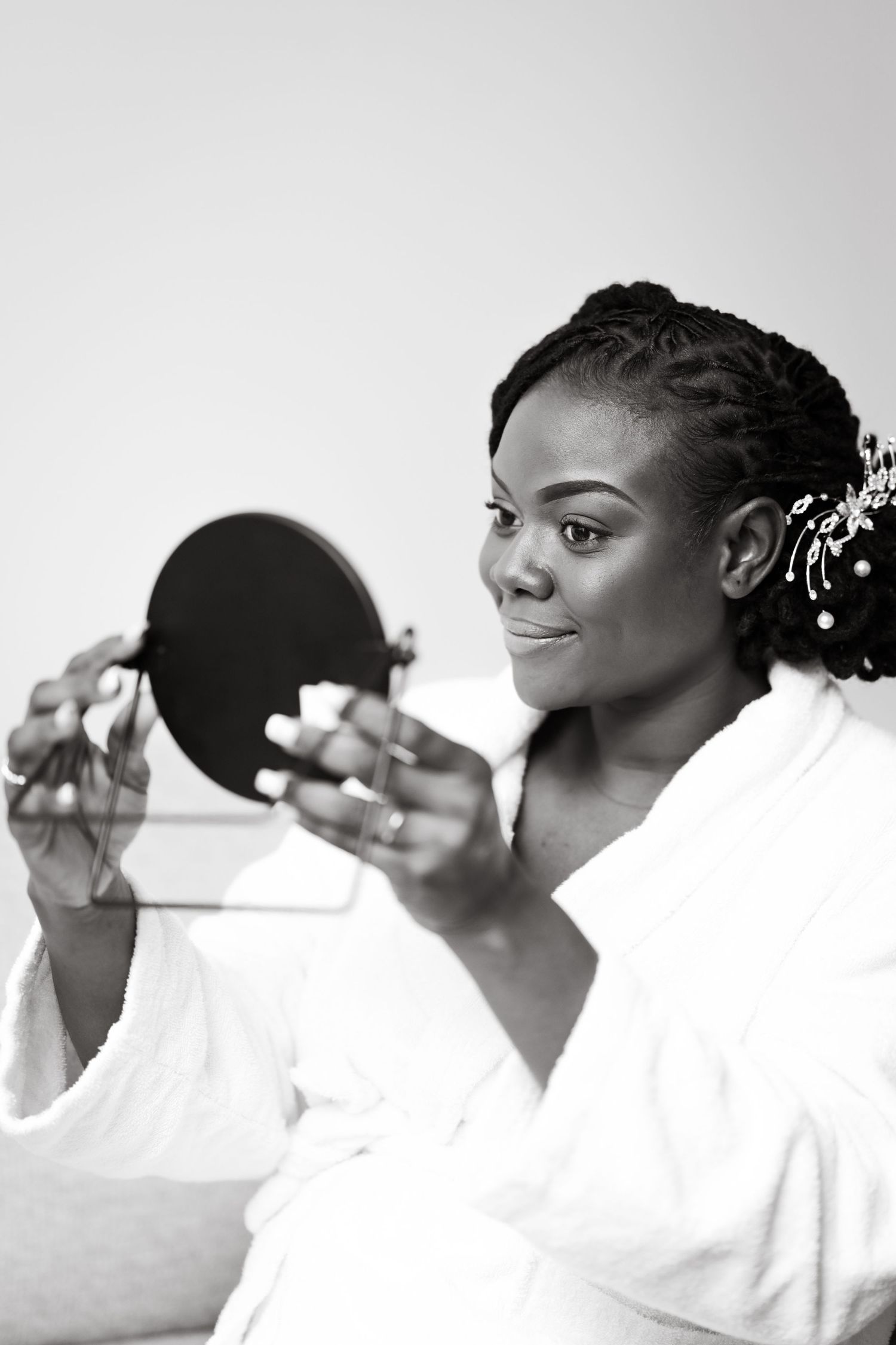 Person in white holding up a compact mirror in artistic black and white photography.