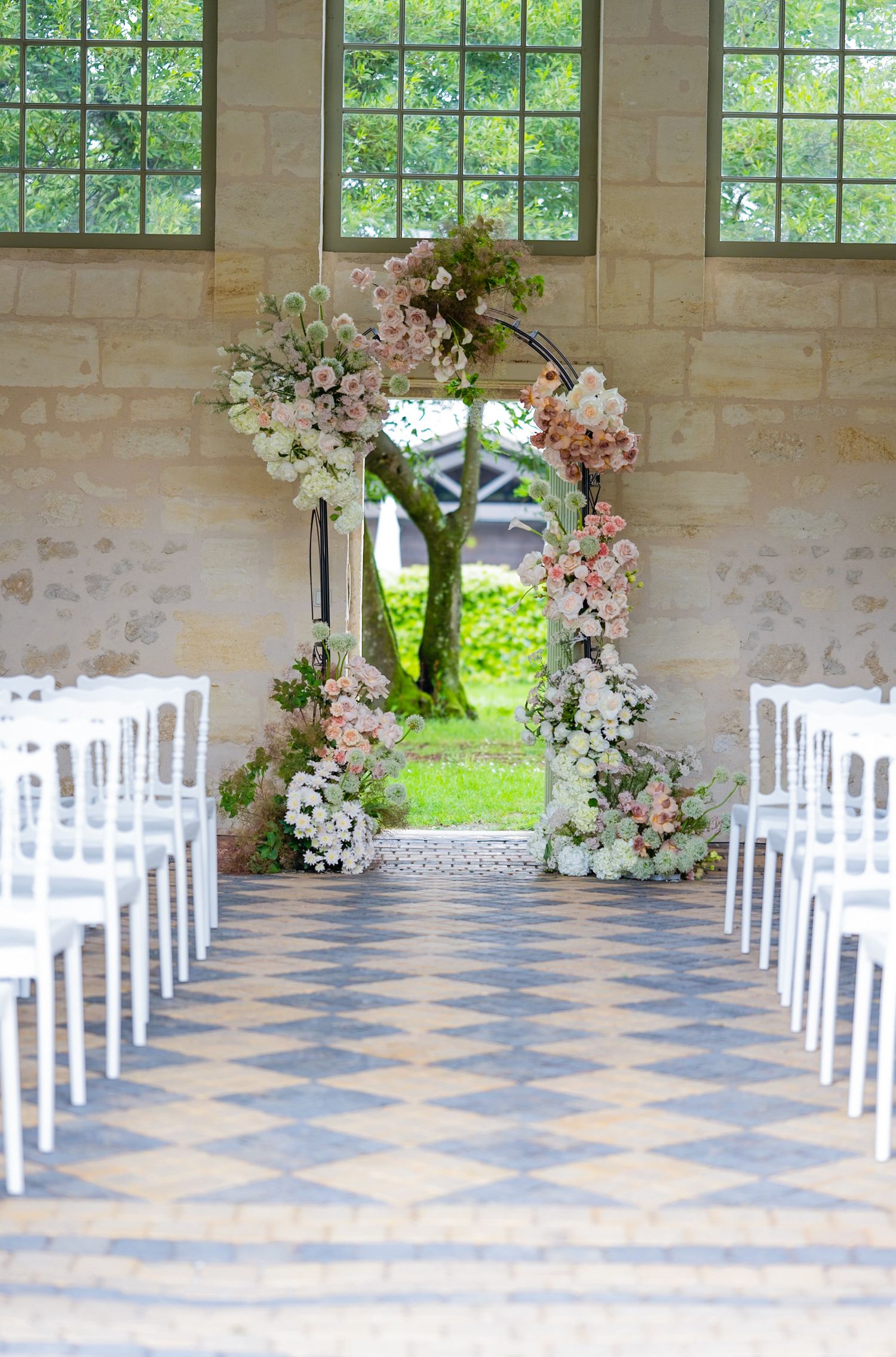 Wedding ceremony venue with floral arch and white chairs in a light-filled room.