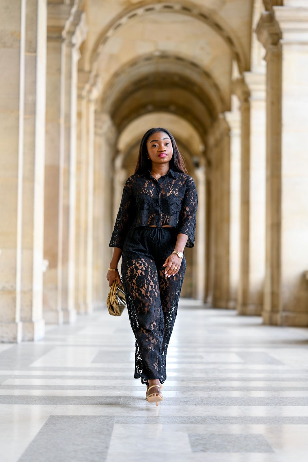 Person in black lace outfit walking through elegant arched stone corridor.