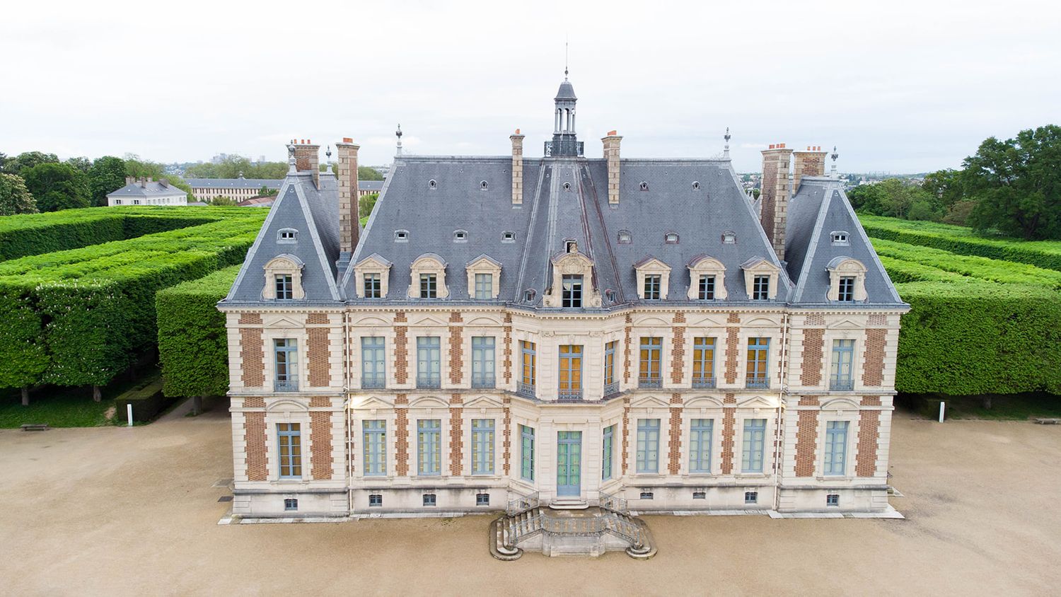 Aerial view of a grand French chateau with symmetrical architecture and manicured gardens.
