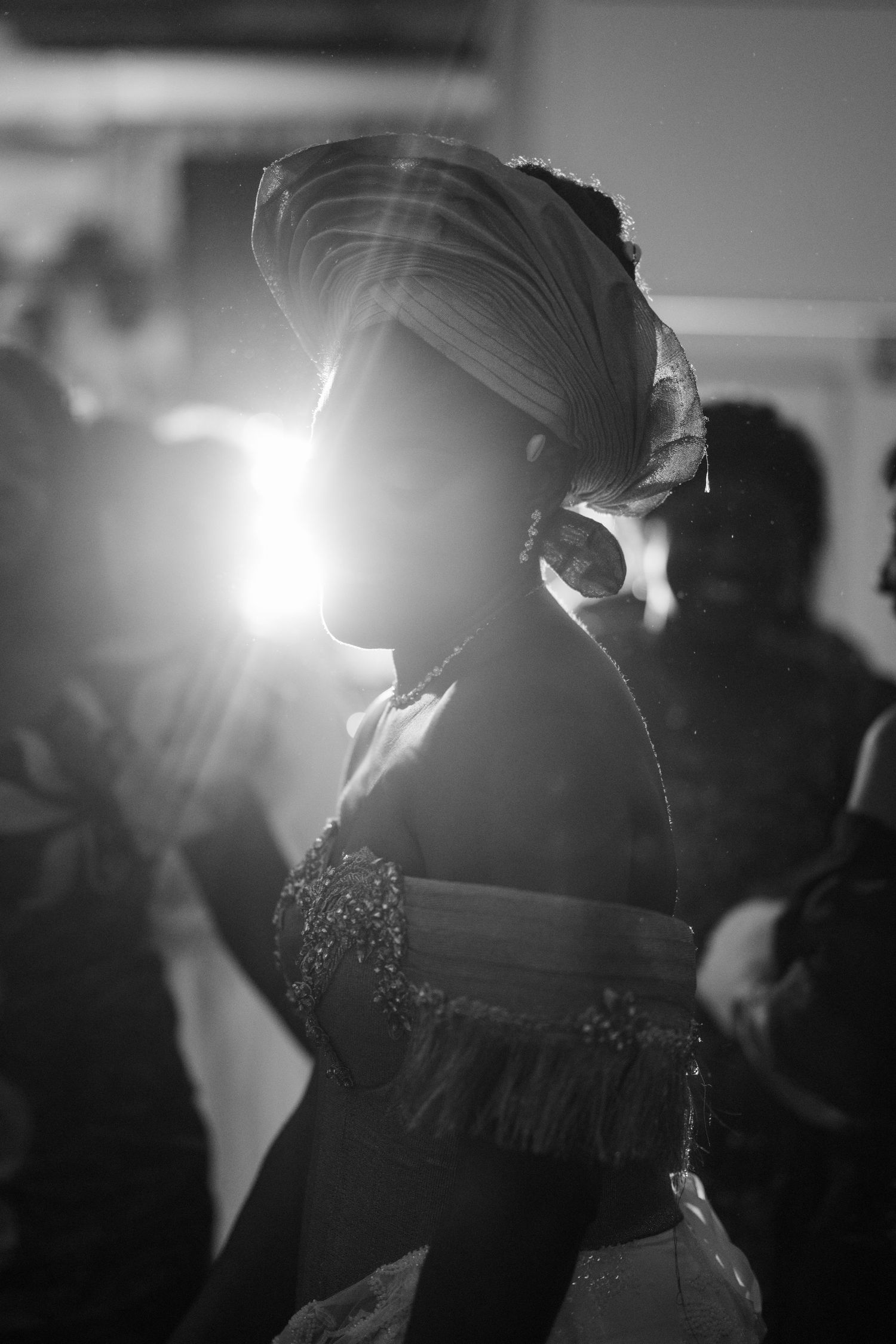 Silhouetted figure in traditional headwrap and formal attire at evening celebration.