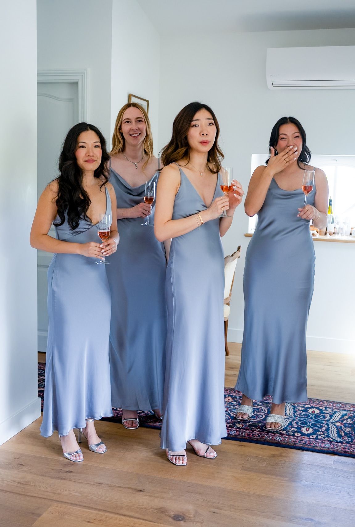 Four bridesmaids in matching dusty blue silk dresses posing together indoors.