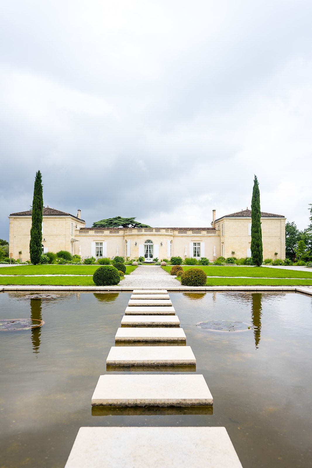 Geometric stepping stones over reflective water leading to an elegant mansion.