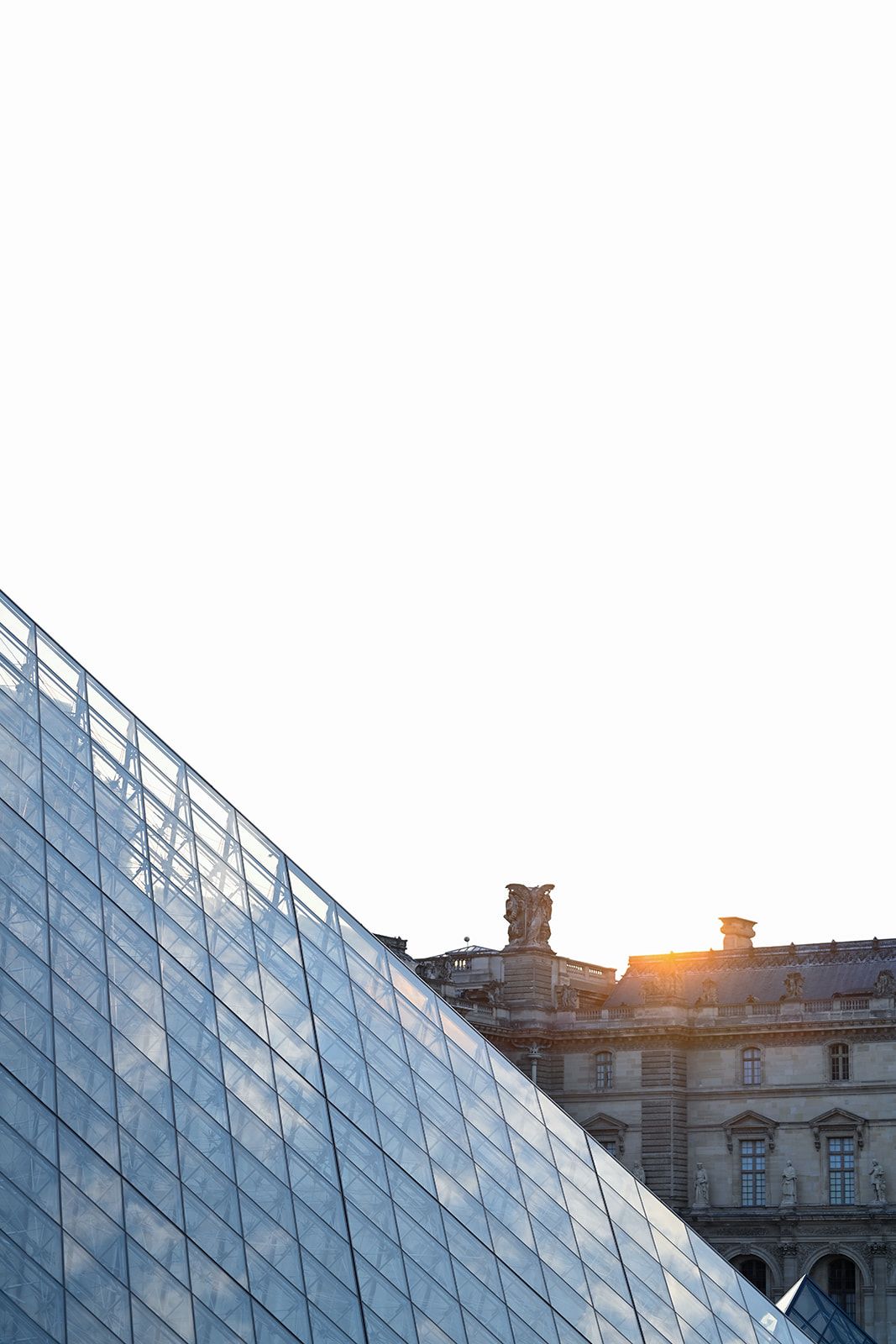 Glass pyramid of the Louvre Museum at sunset with historic building facade in background.