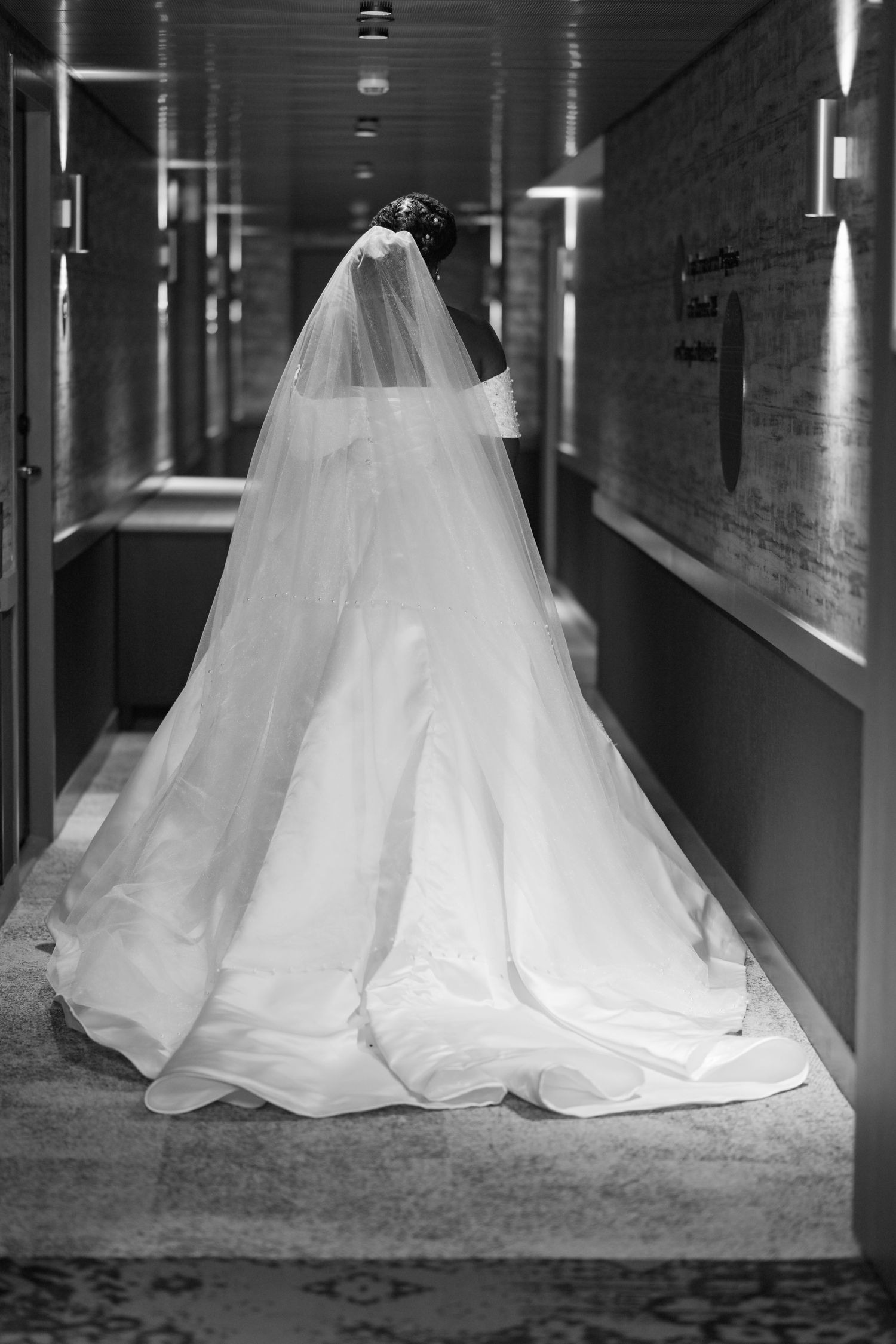 Back view of a flowing white wedding gown with long train in a hallway.
